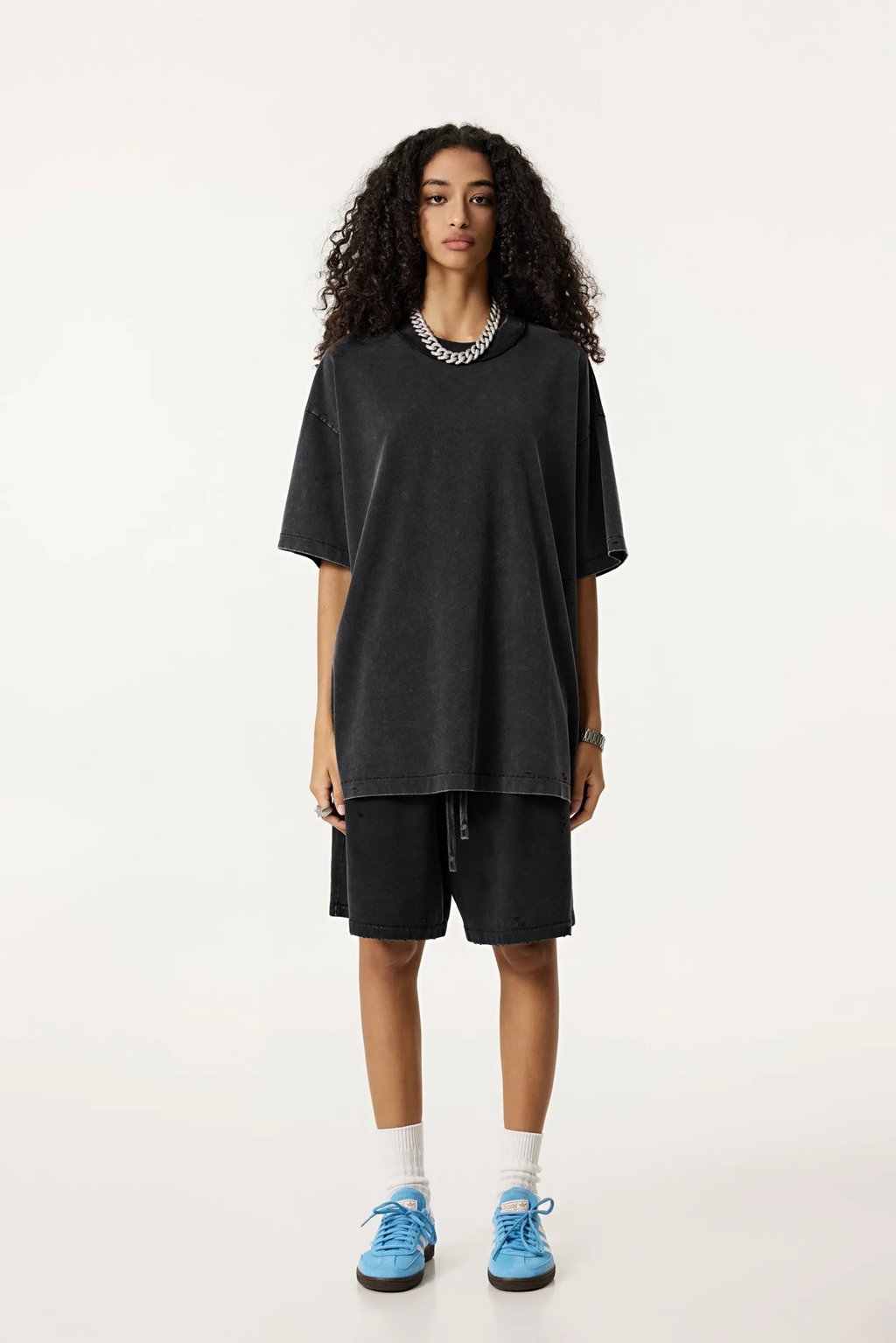 Person wearing a black oversized t-shirt and shorts set with blue sneakers on a white background