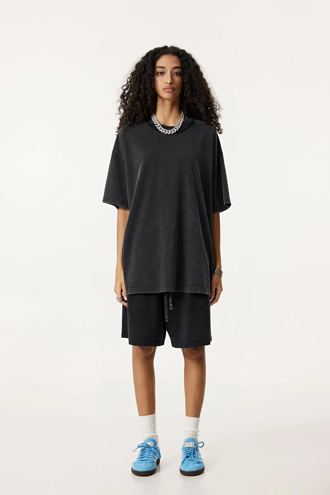 Person wearing a black oversized t-shirt and shorts set with blue sneakers on a white background