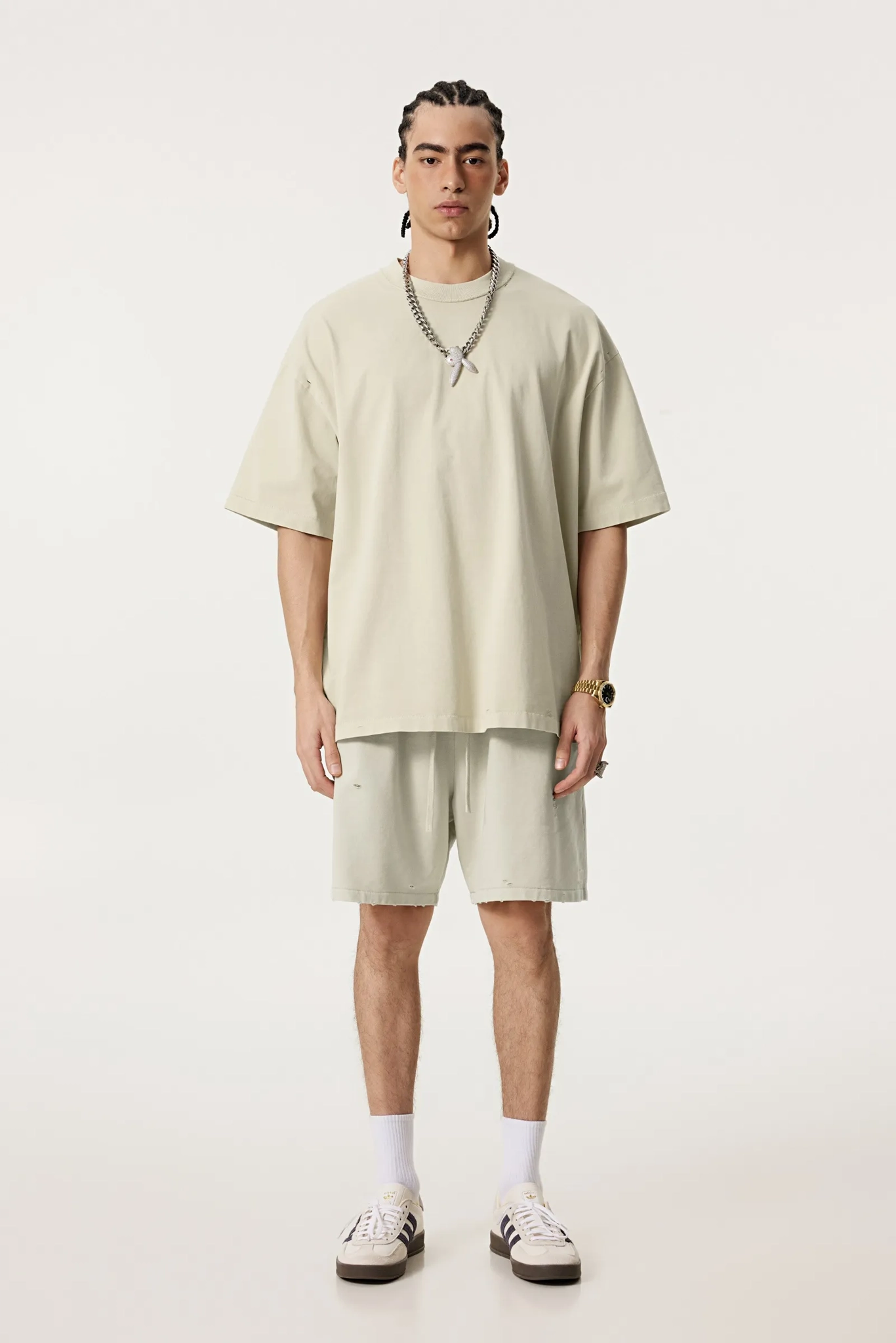 Person wearing a beige oversized t-shirt and shorts set on a white background