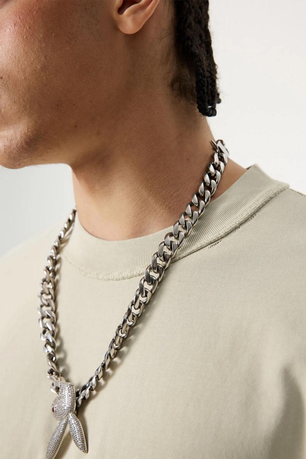 Person wearing a silver chain necklace with a leaf pendant on a plain background