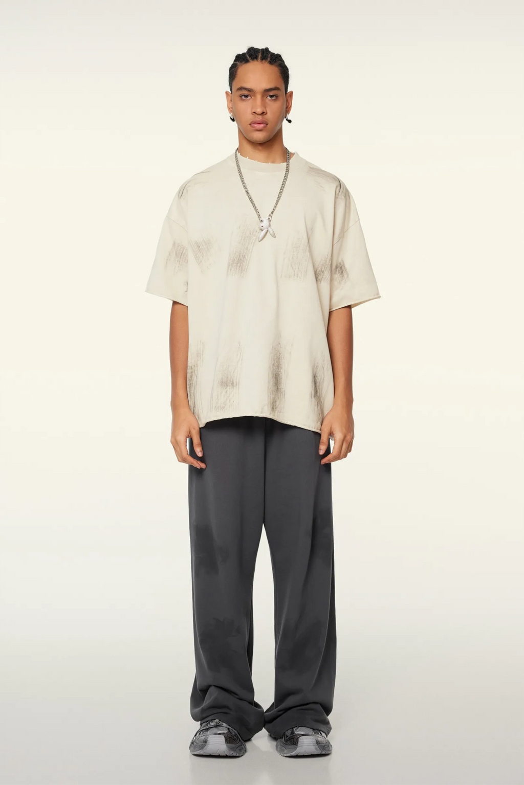 Person wearing a beige oversized shirt and gray pants on a white background