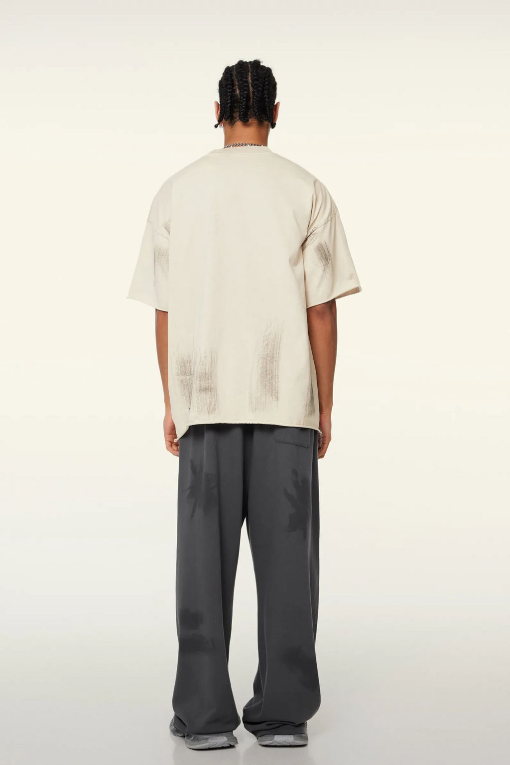 Person wearing a beige oversized t-shirt and gray pants on a white background