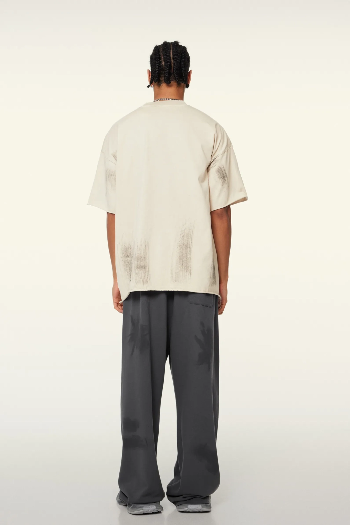 Person wearing a beige oversized t-shirt and gray pants on a white background