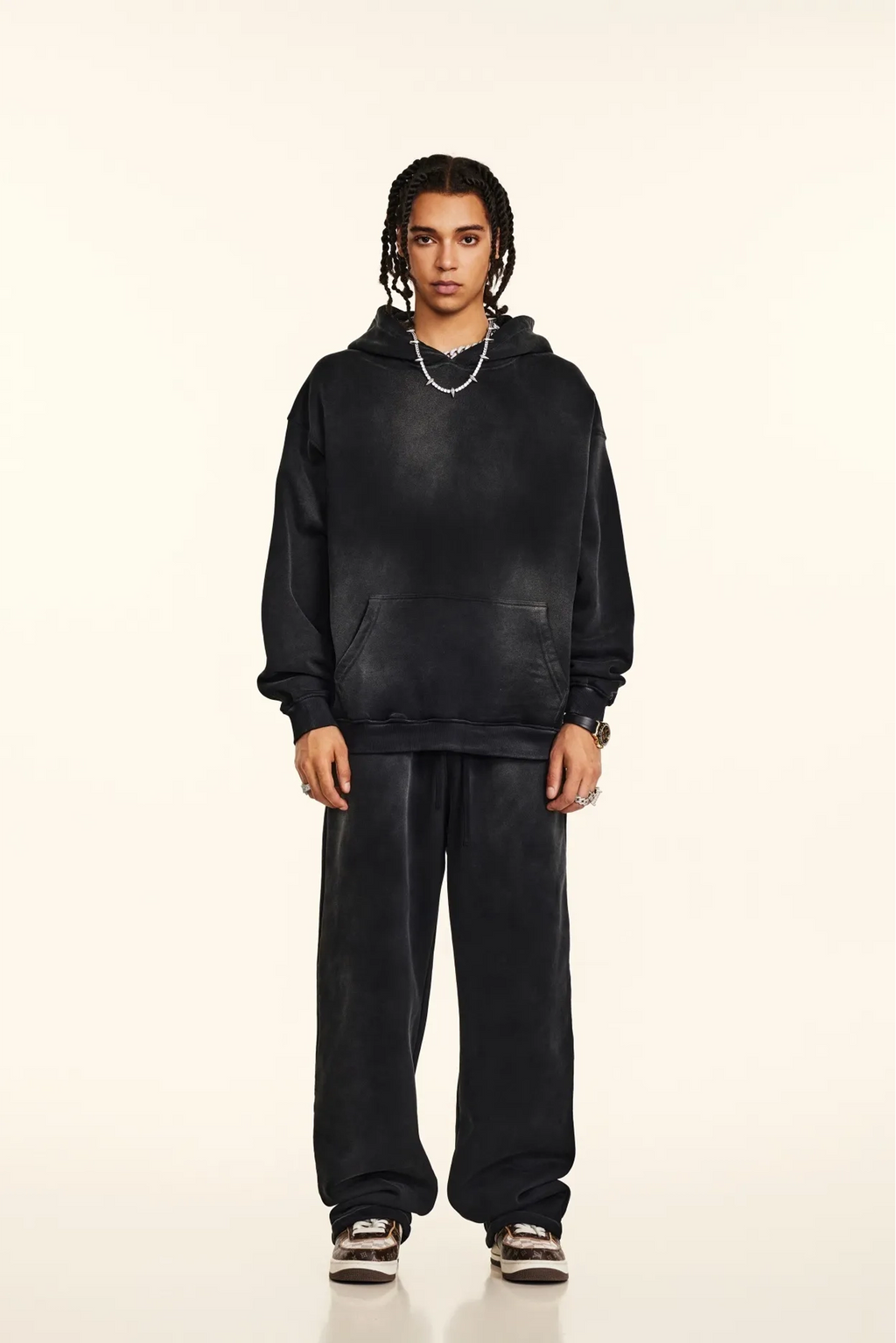 Person wearing a black hoodie and pants on a beige background