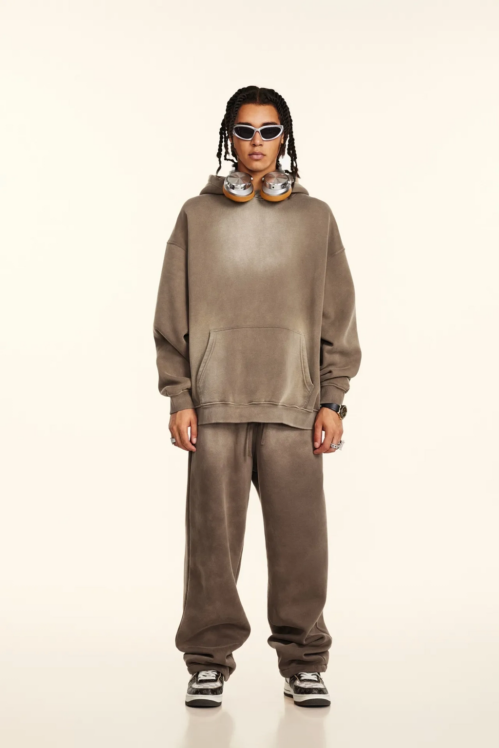 Person wearing a brown tracksuit with sunglasses on a white background