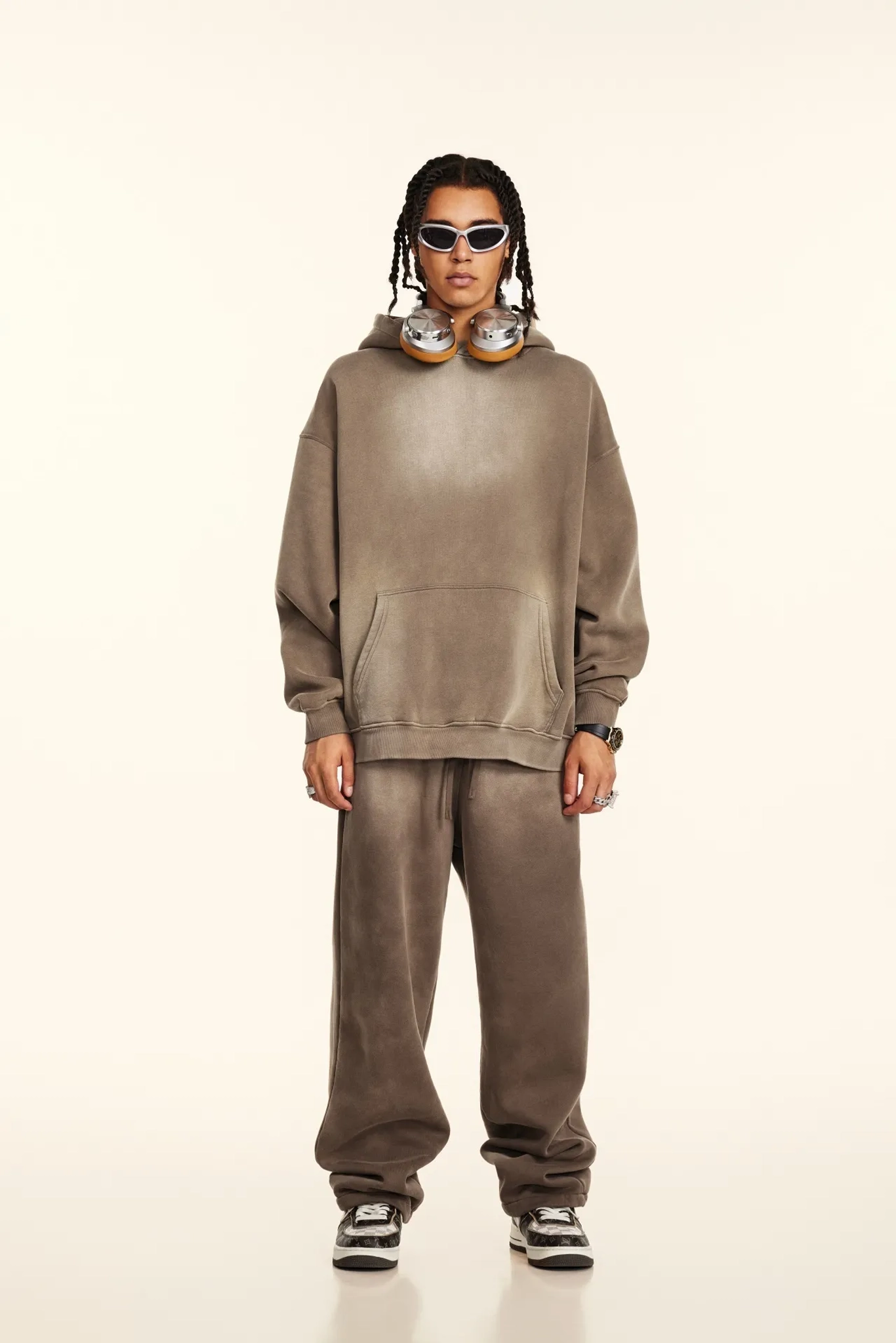 Person wearing a brown tracksuit with sunglasses on a white background