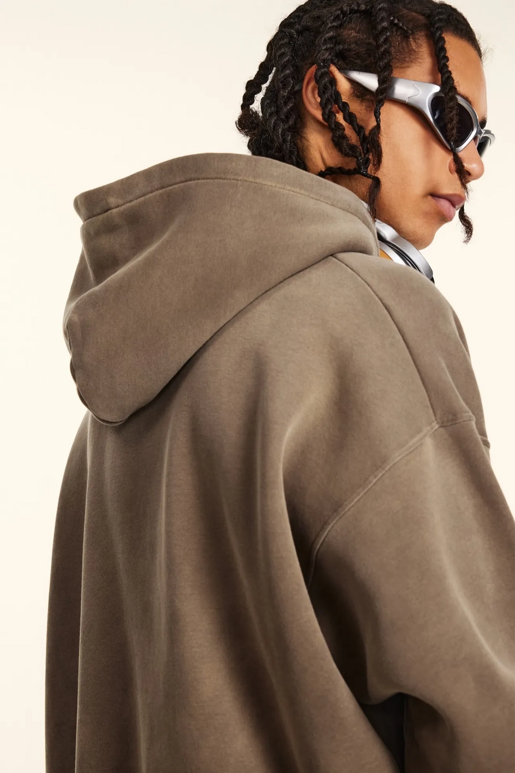 Person wearing a brown hoodie and sunglasses on a plain background