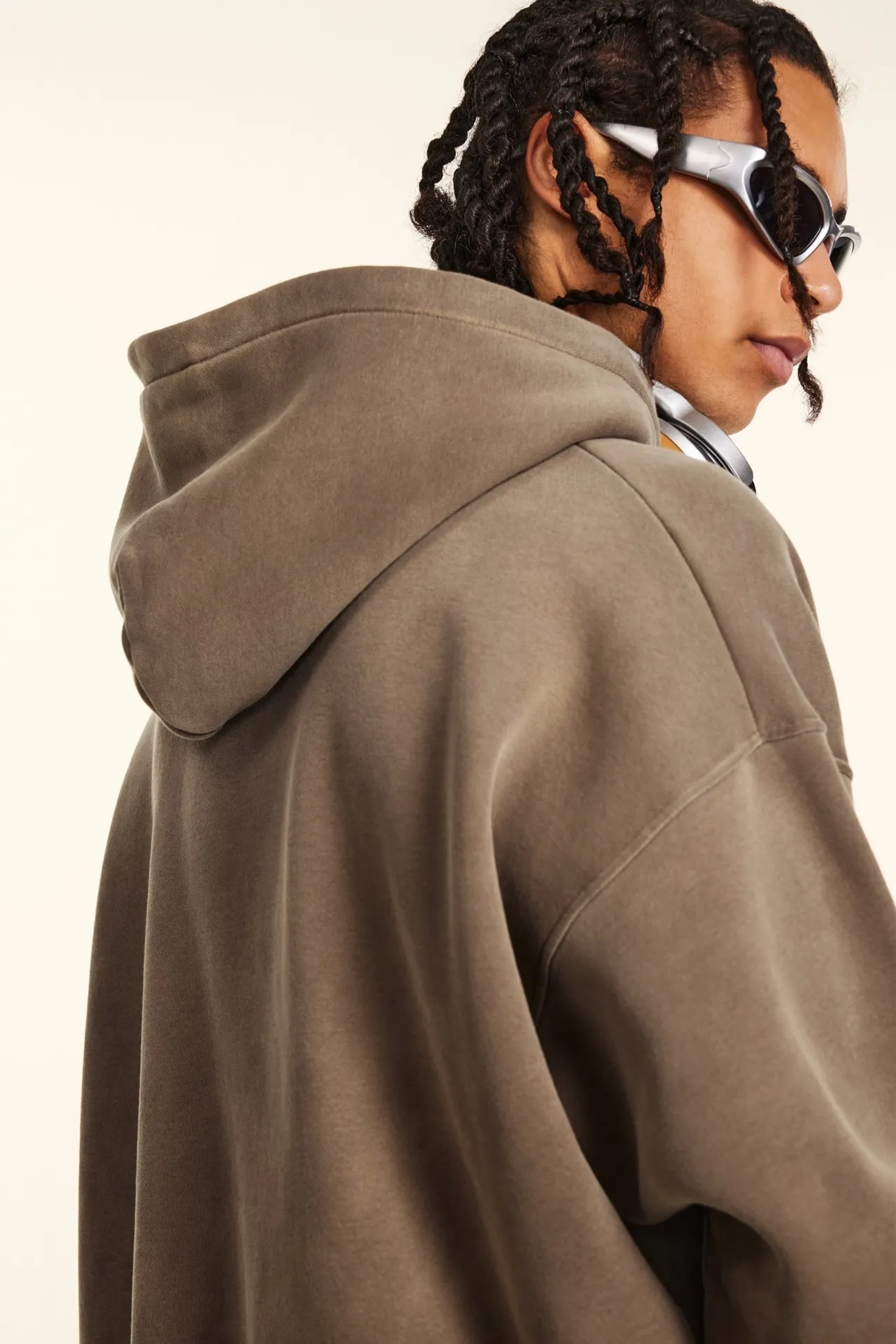 Person wearing a brown hoodie and sunglasses on a plain background