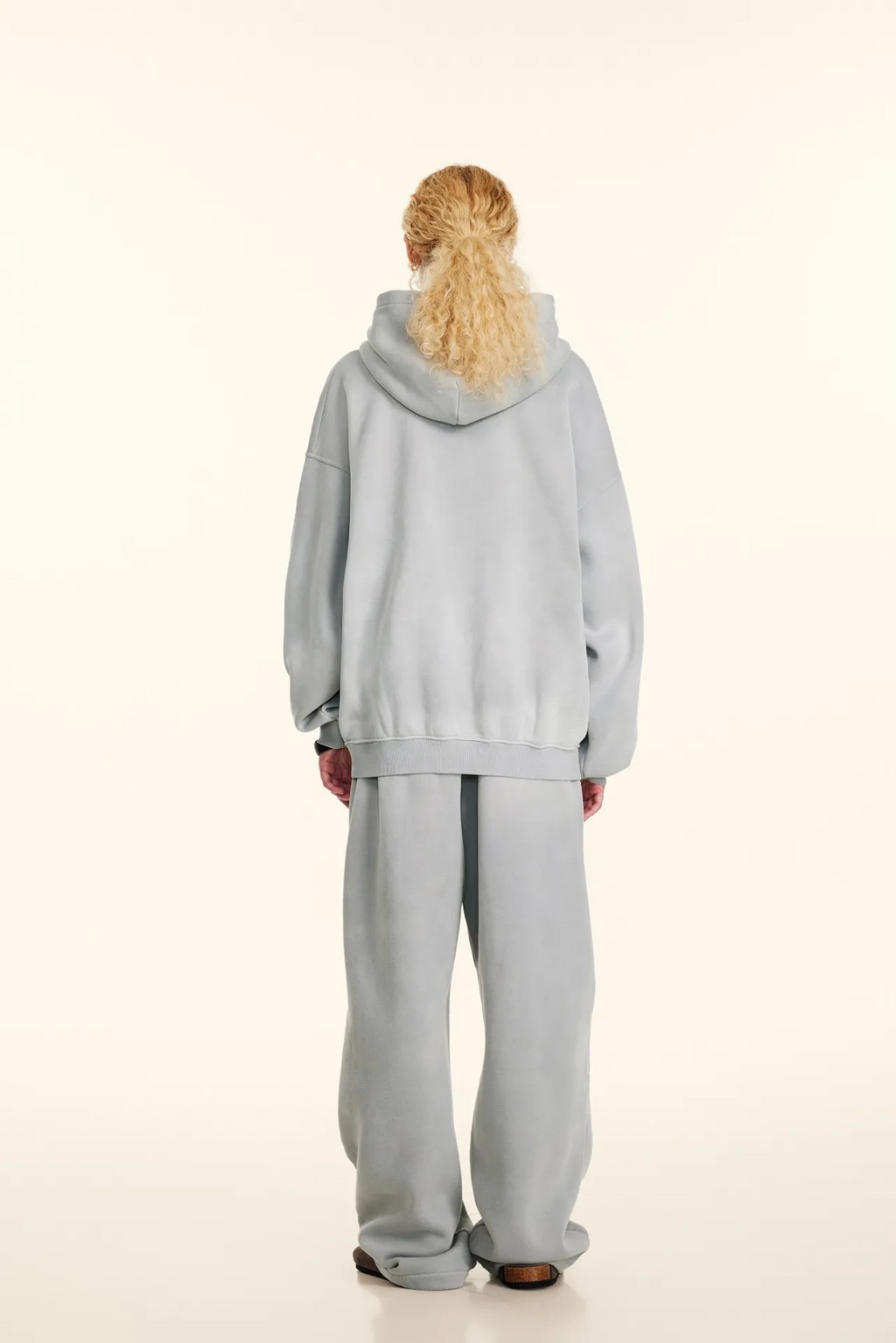 Person wearing a light gray hoodie and pants on a white background