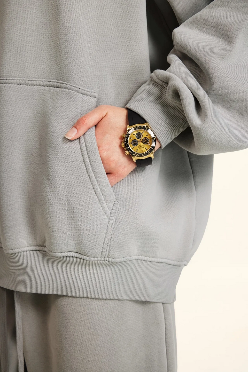 Person wearing a gray hoodie with a gold watch on a light background