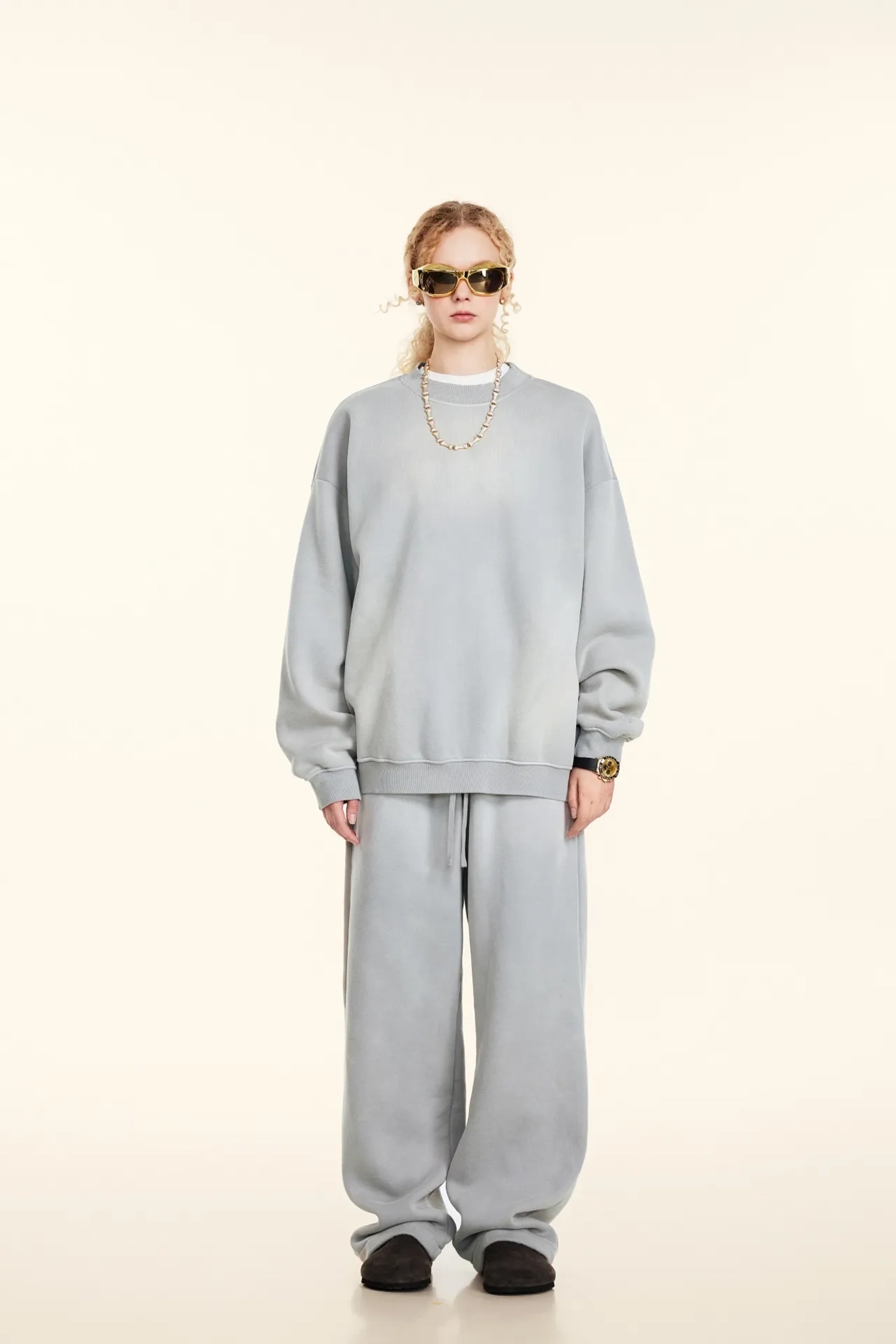 Person wearing a gray tracksuit with sunglasses on a white background