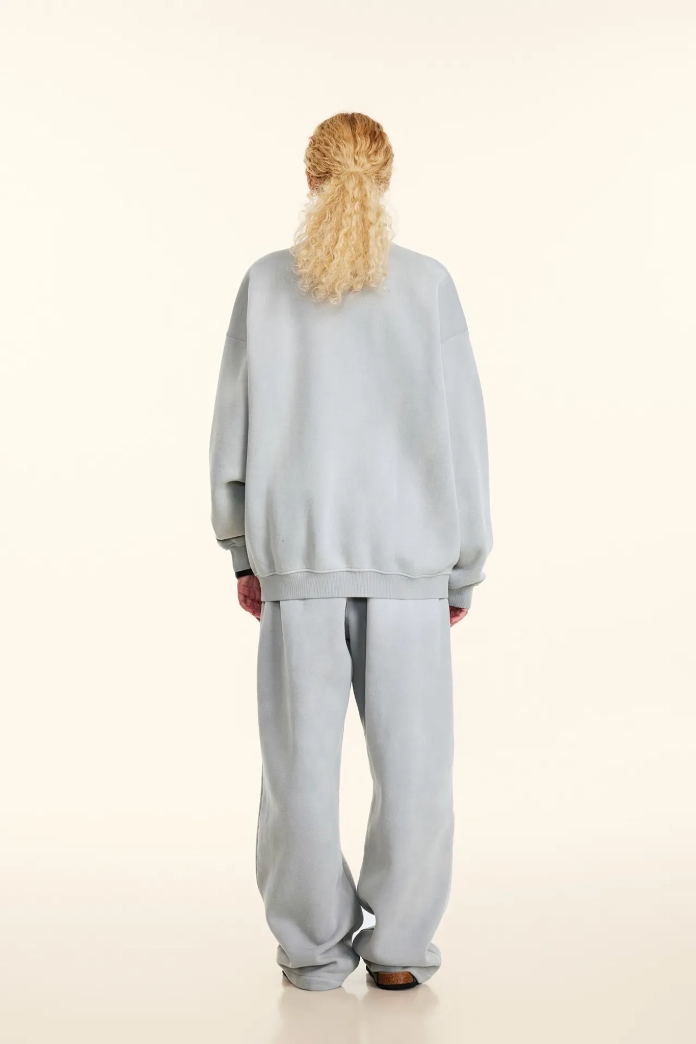 Person wearing a light gray tracksuit on a white background