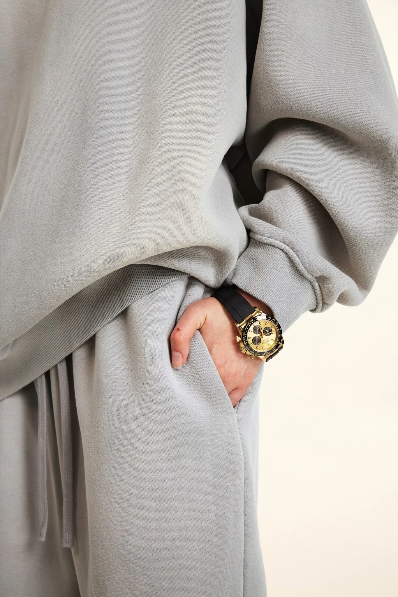Person wearing a light gray coat with a hand in a pocket, wearing a gold watch.