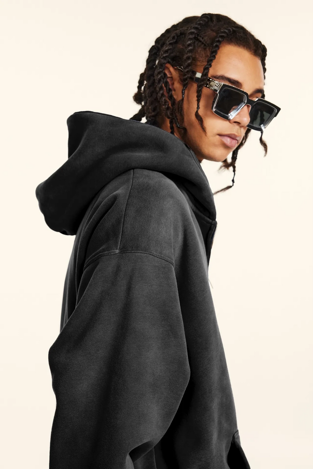 Person wearing a black hoodie and sunglasses on a plain background