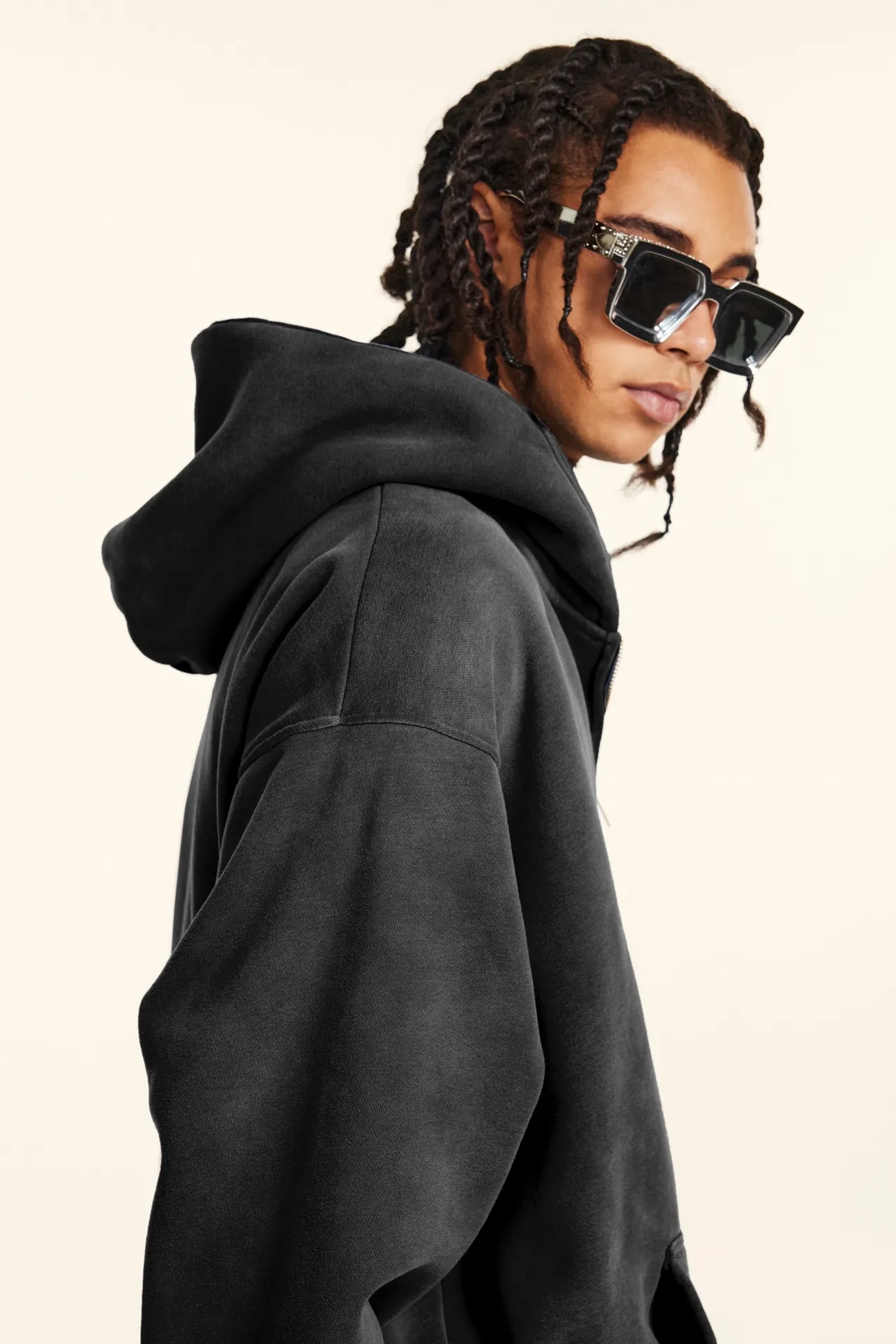 Person wearing a black hoodie and sunglasses on a plain background