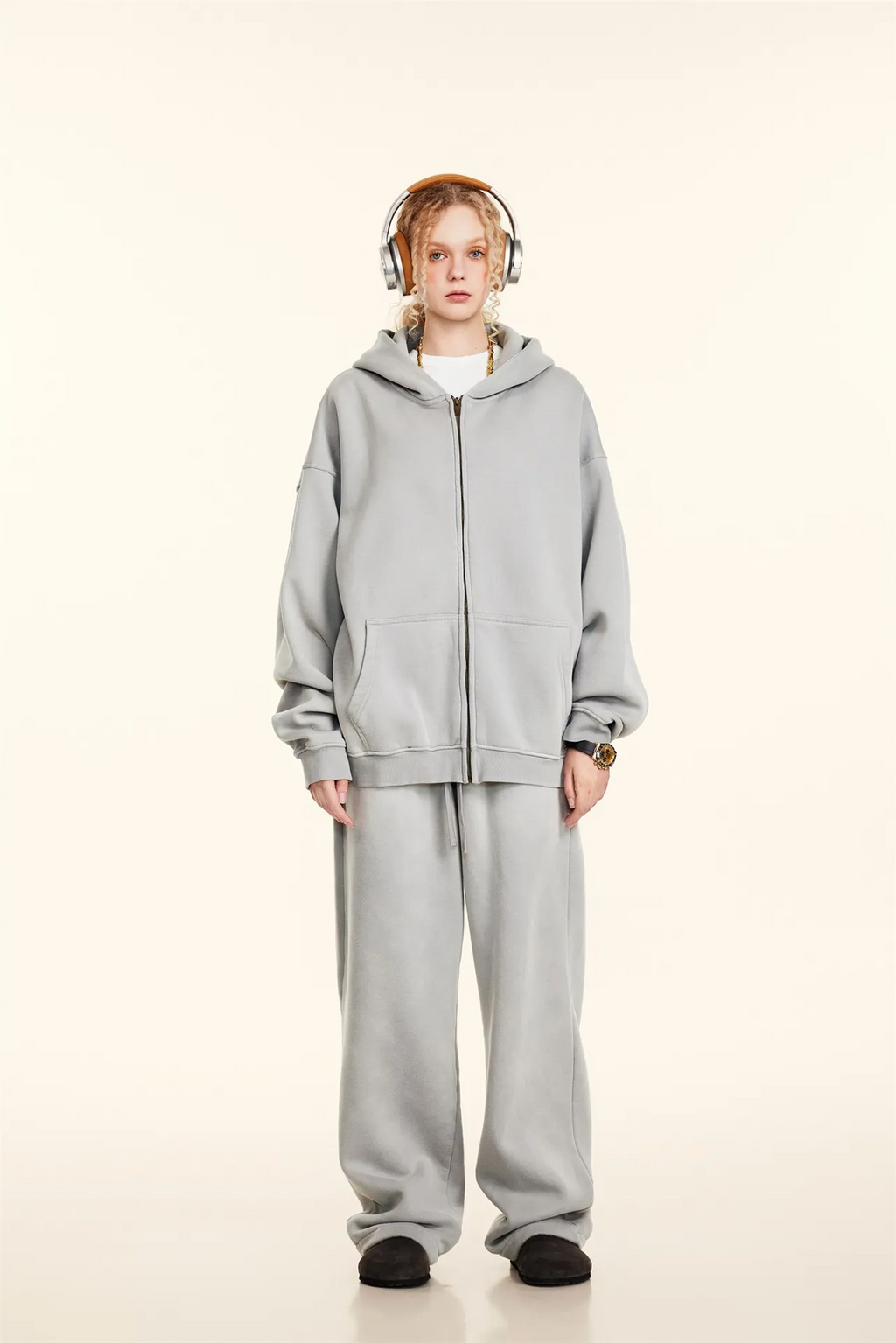 Person wearing a gray tracksuit with headphones on a white background