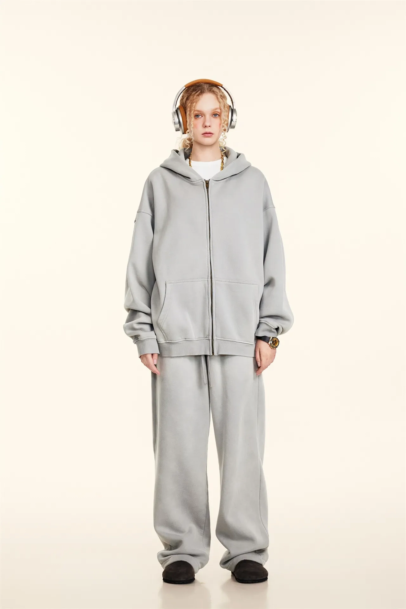 Person wearing a gray tracksuit with headphones on a white background