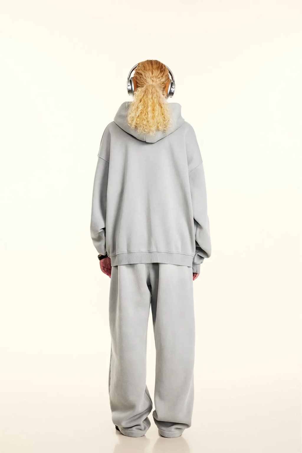 Person wearing a gray tracksuit with headphones on a white background