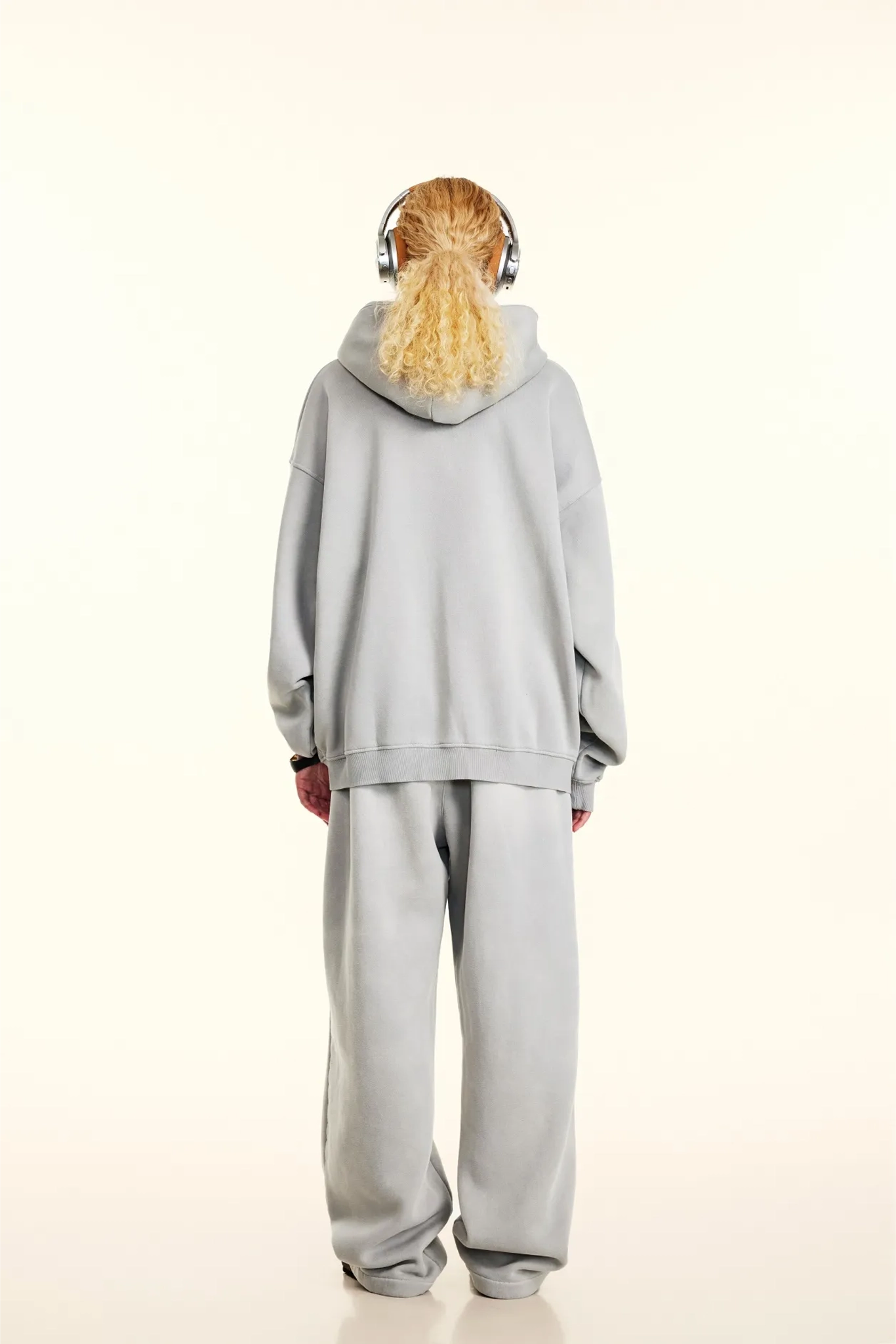 Person wearing a gray tracksuit with headphones on a white background