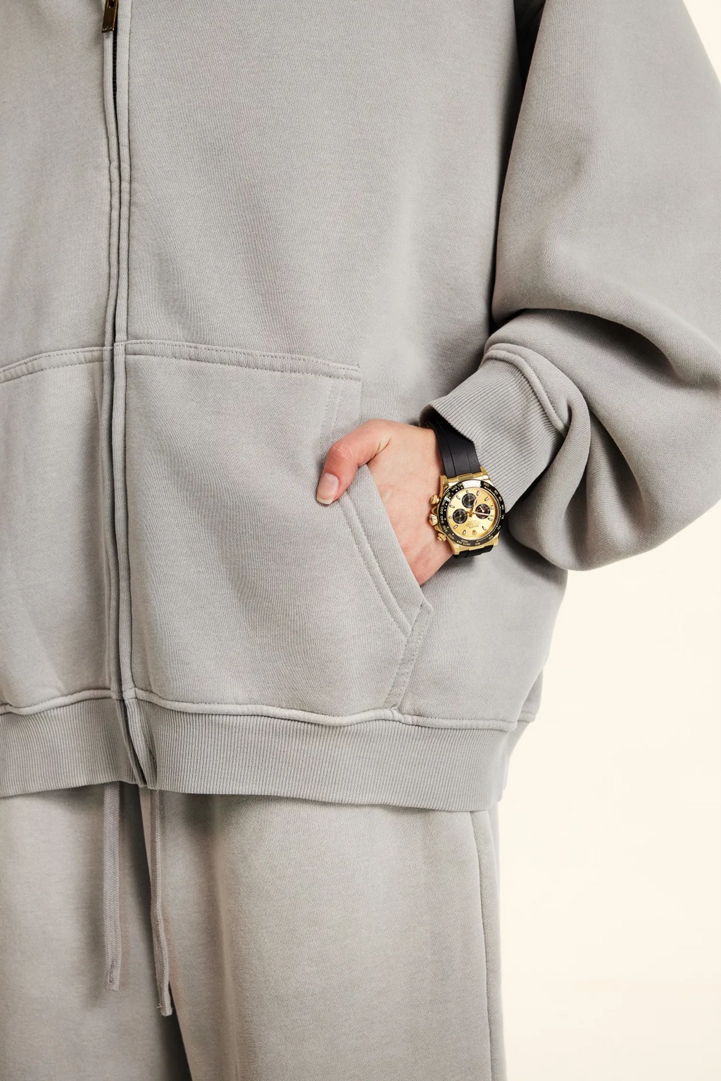Person wearing a gray tracksuit with a gold watch on a light background