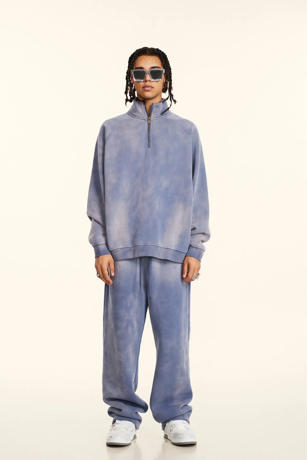 Person wearing a blue tie-dye outfit with sunglasses on a white background