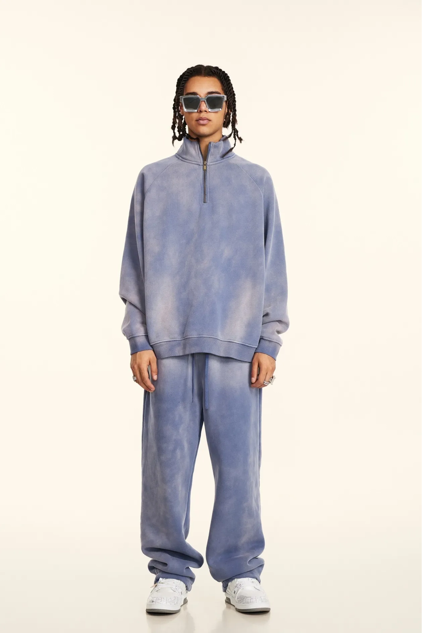 Person wearing a blue tie-dye outfit with sunglasses on a white background
