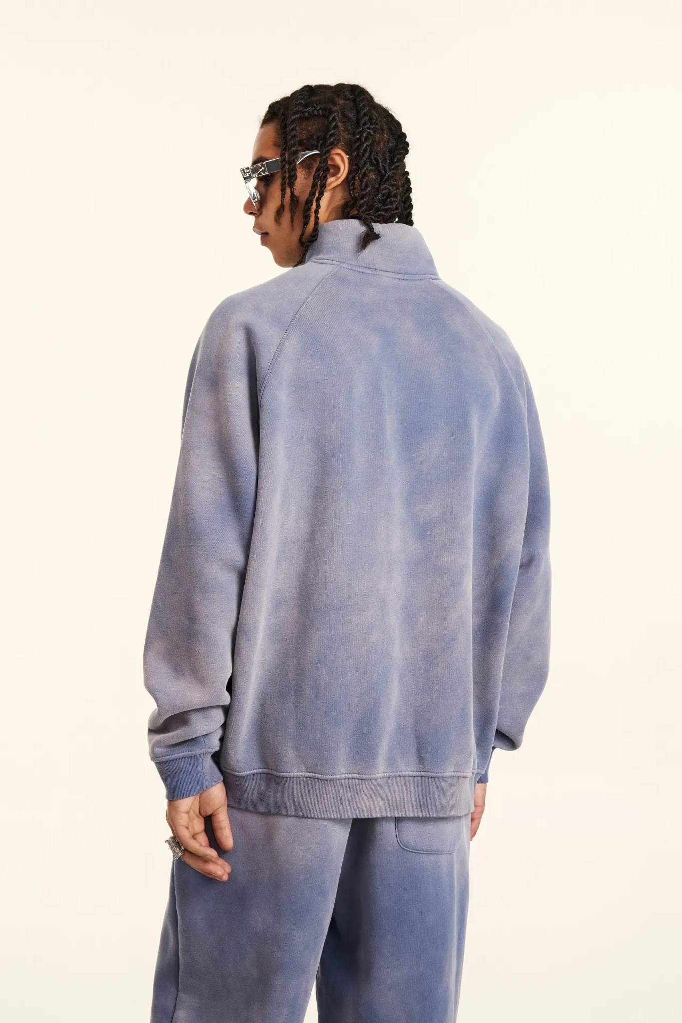 Person wearing a blue tie-dye tracksuit from behind on a white background