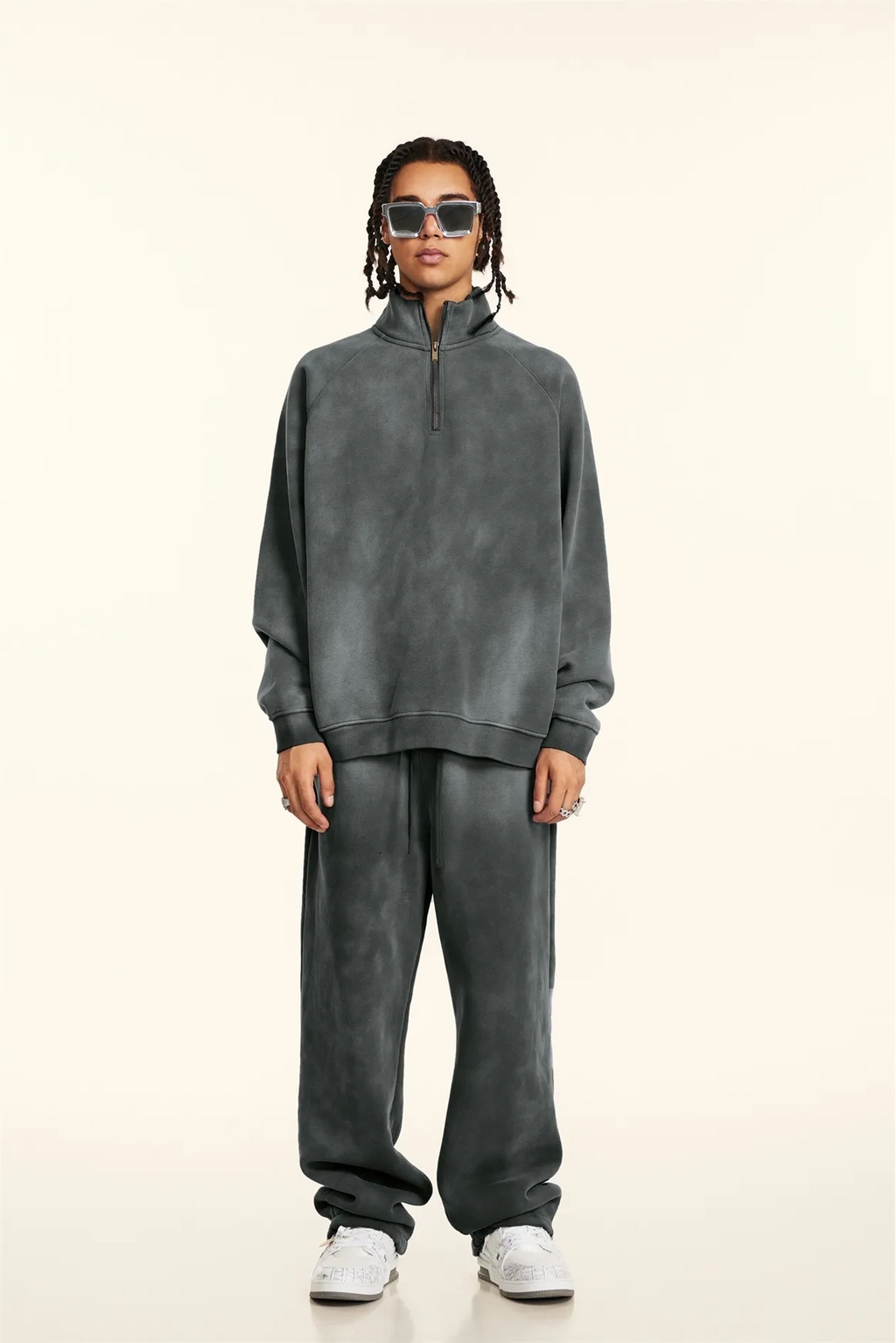 Person wearing a gray tracksuit and sunglasses on a white background