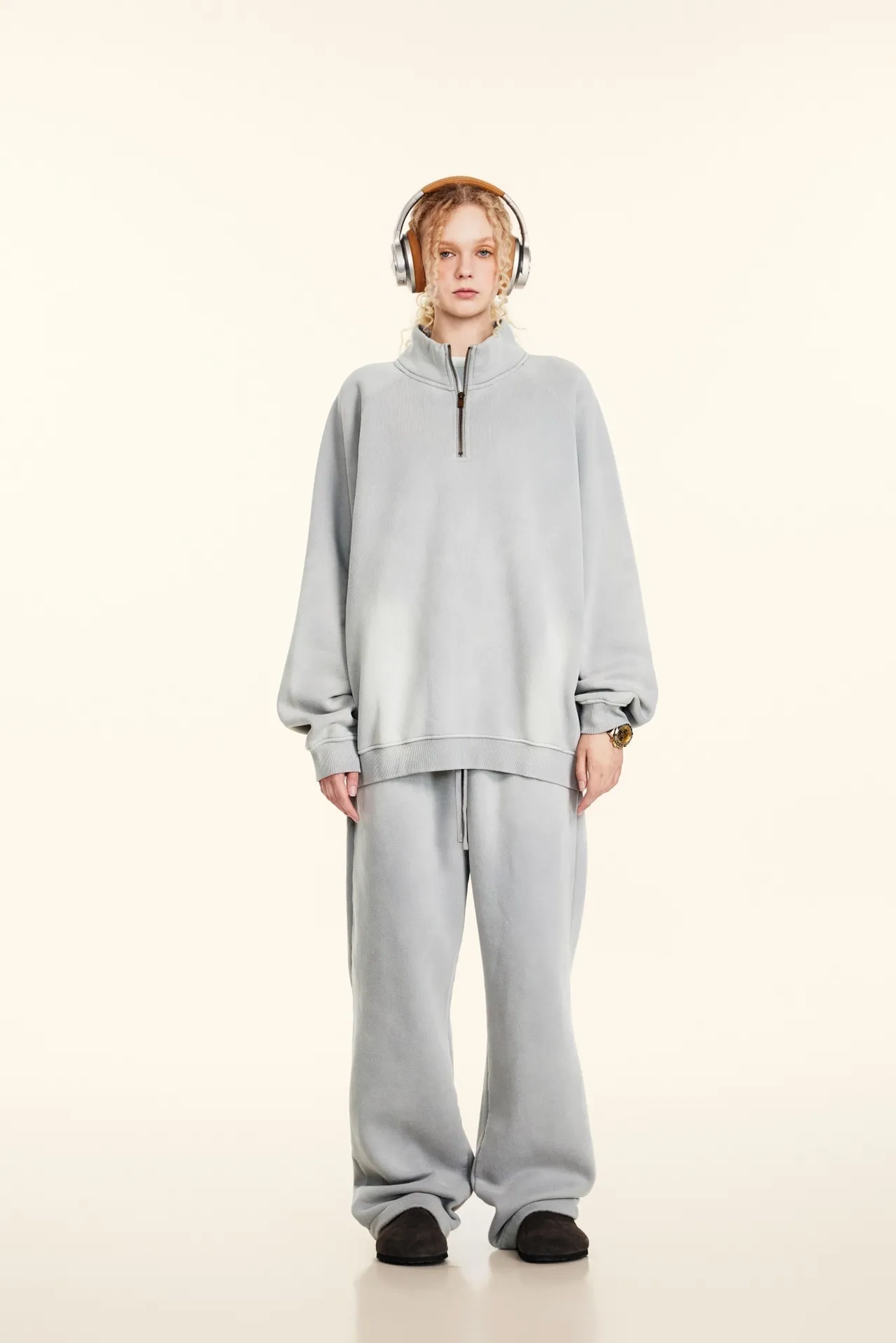 Person wearing a gray tracksuit and headphones on a white background