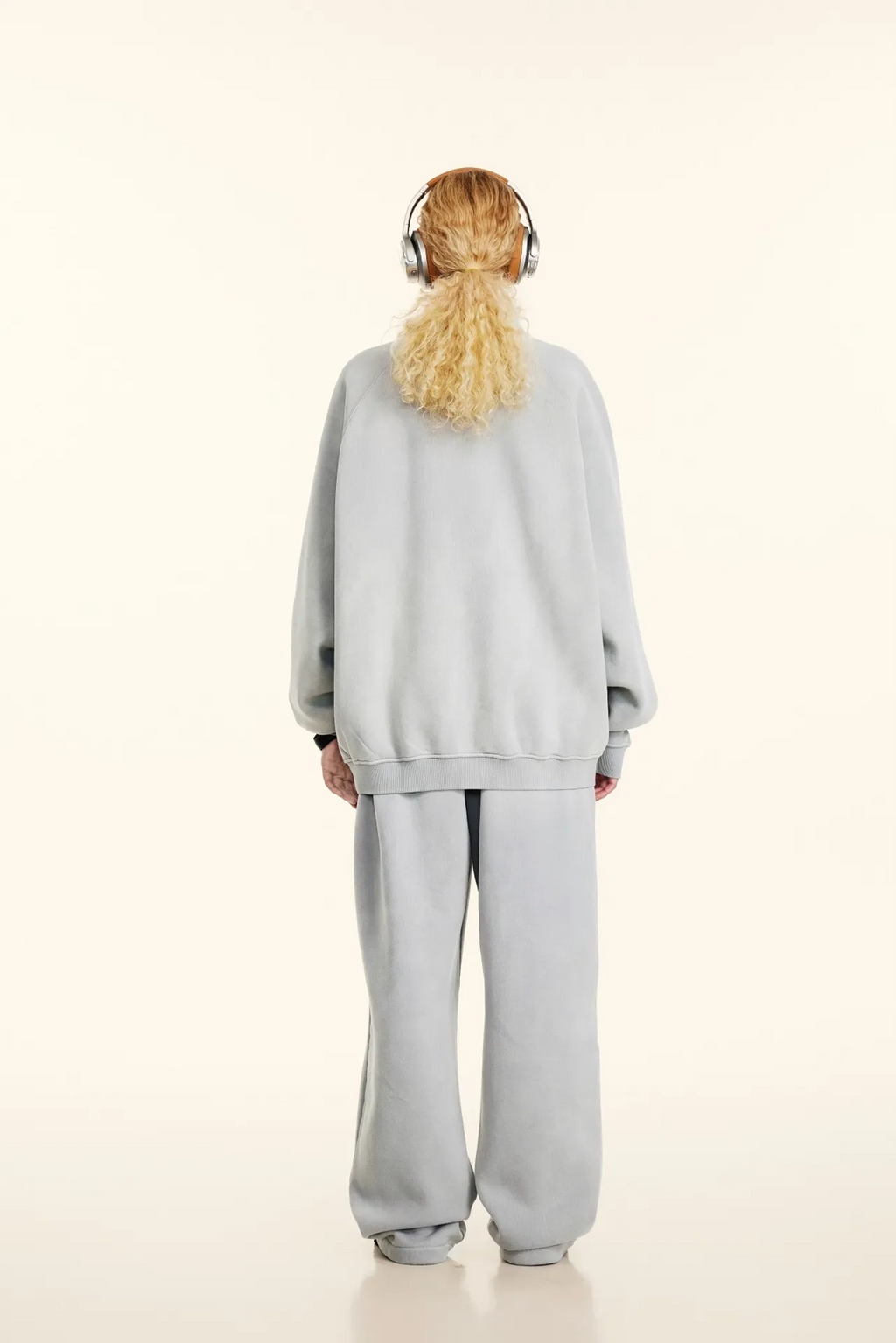 Person wearing a light gray tracksuit and headphones on a white background