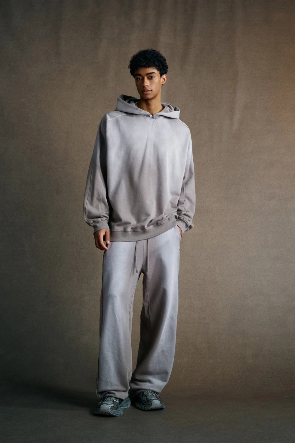 Person wearing a gray hoodie and pants against a plain background