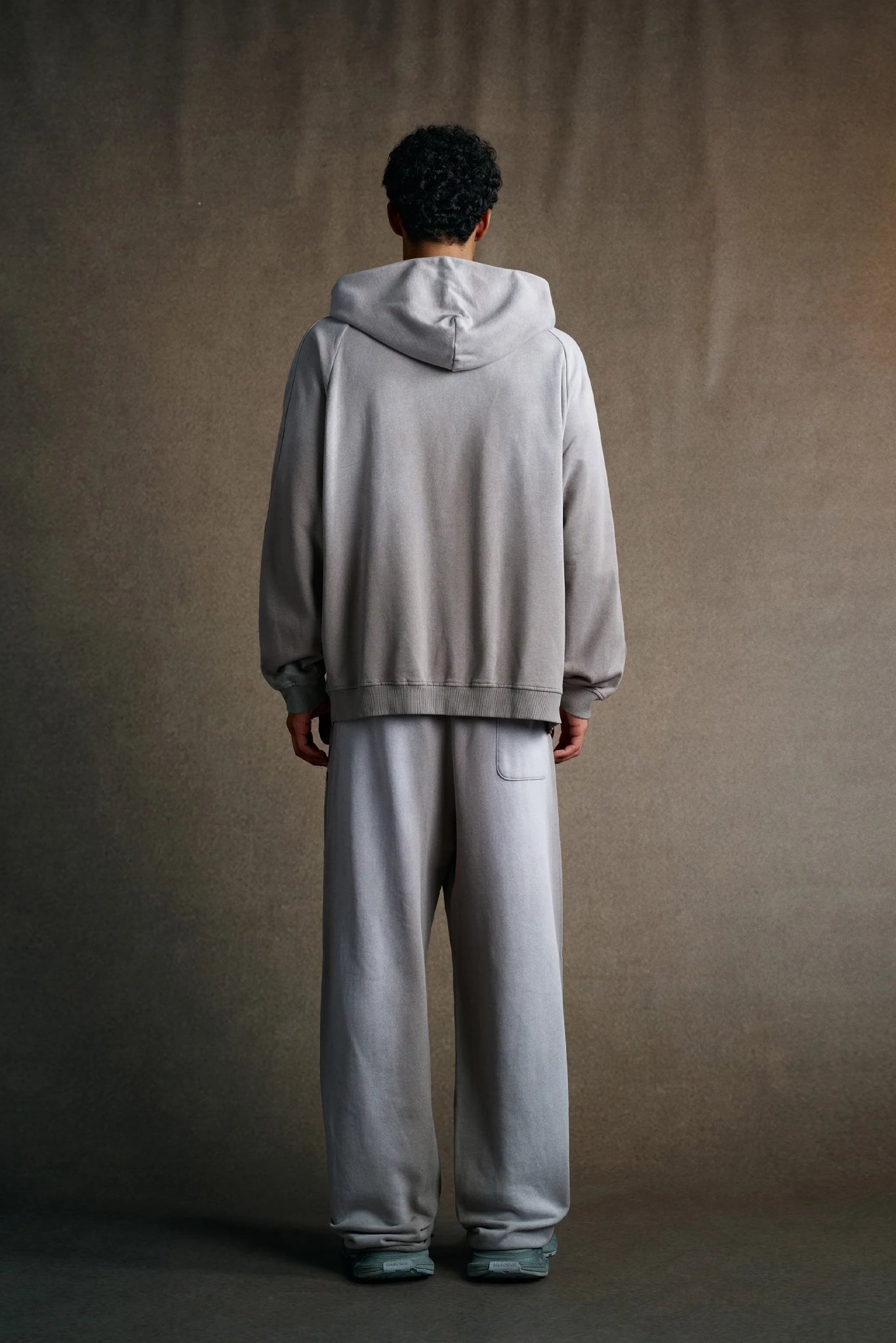 Person wearing a light gray hoodie and pants against a plain background