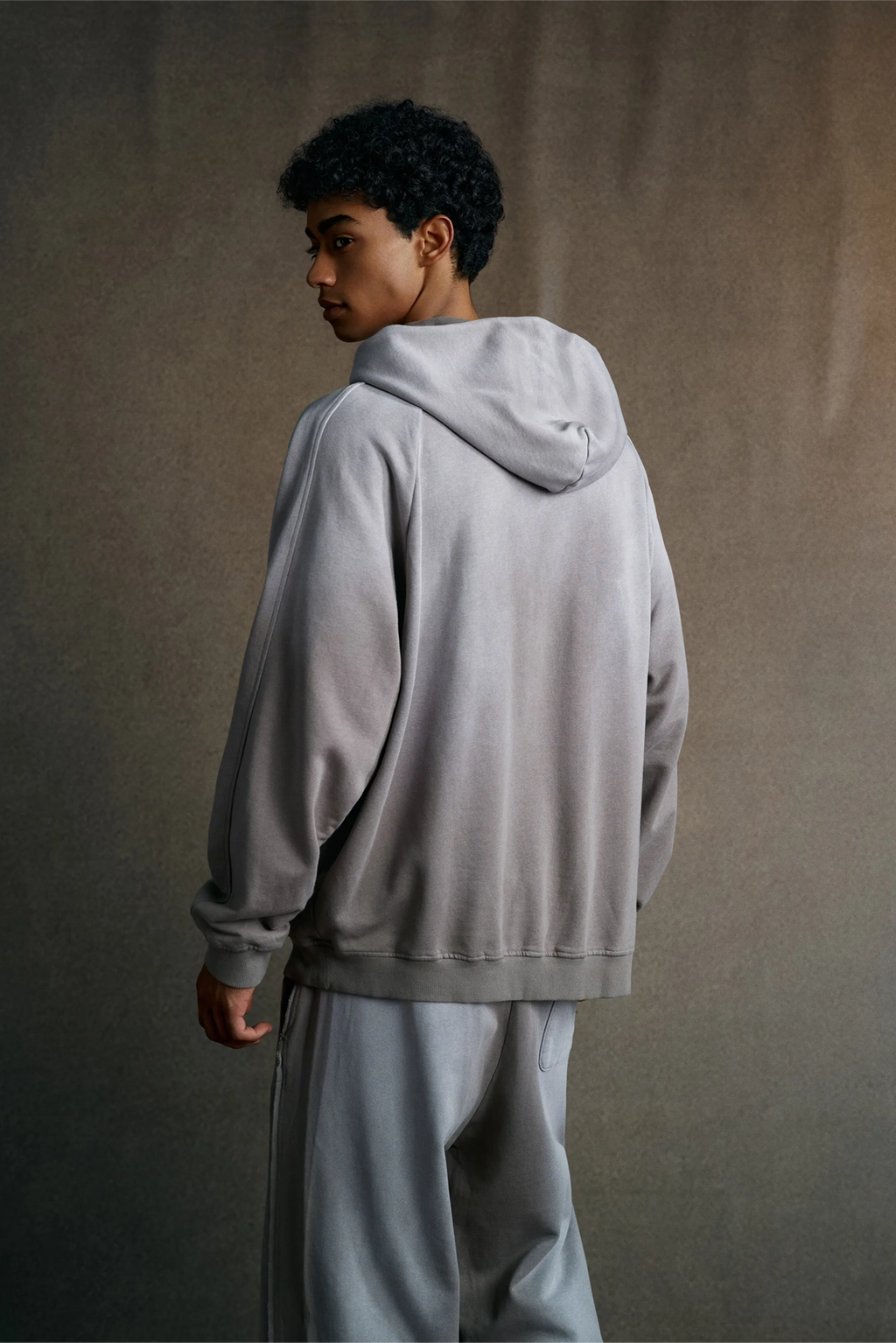 Person wearing a gray hoodie and pants against a plain background