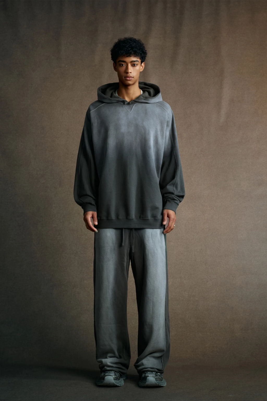 Person wearing a gray hoodie and pants against a brown background