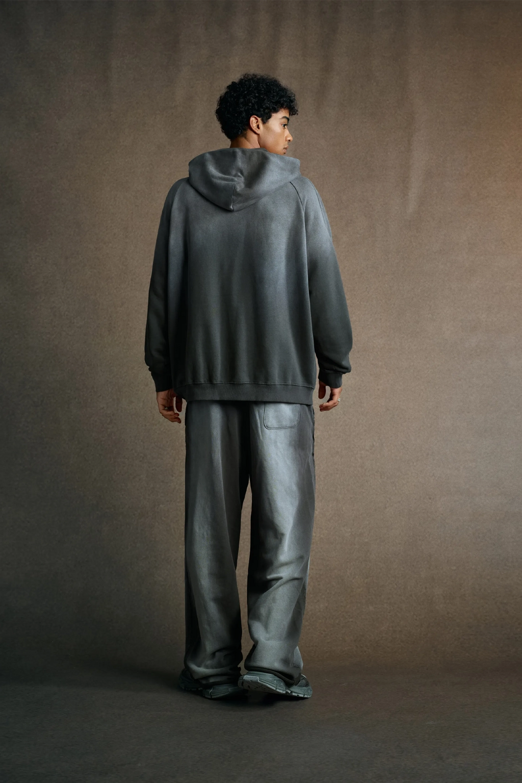 Person wearing a gray hoodie and pants against a brown background
