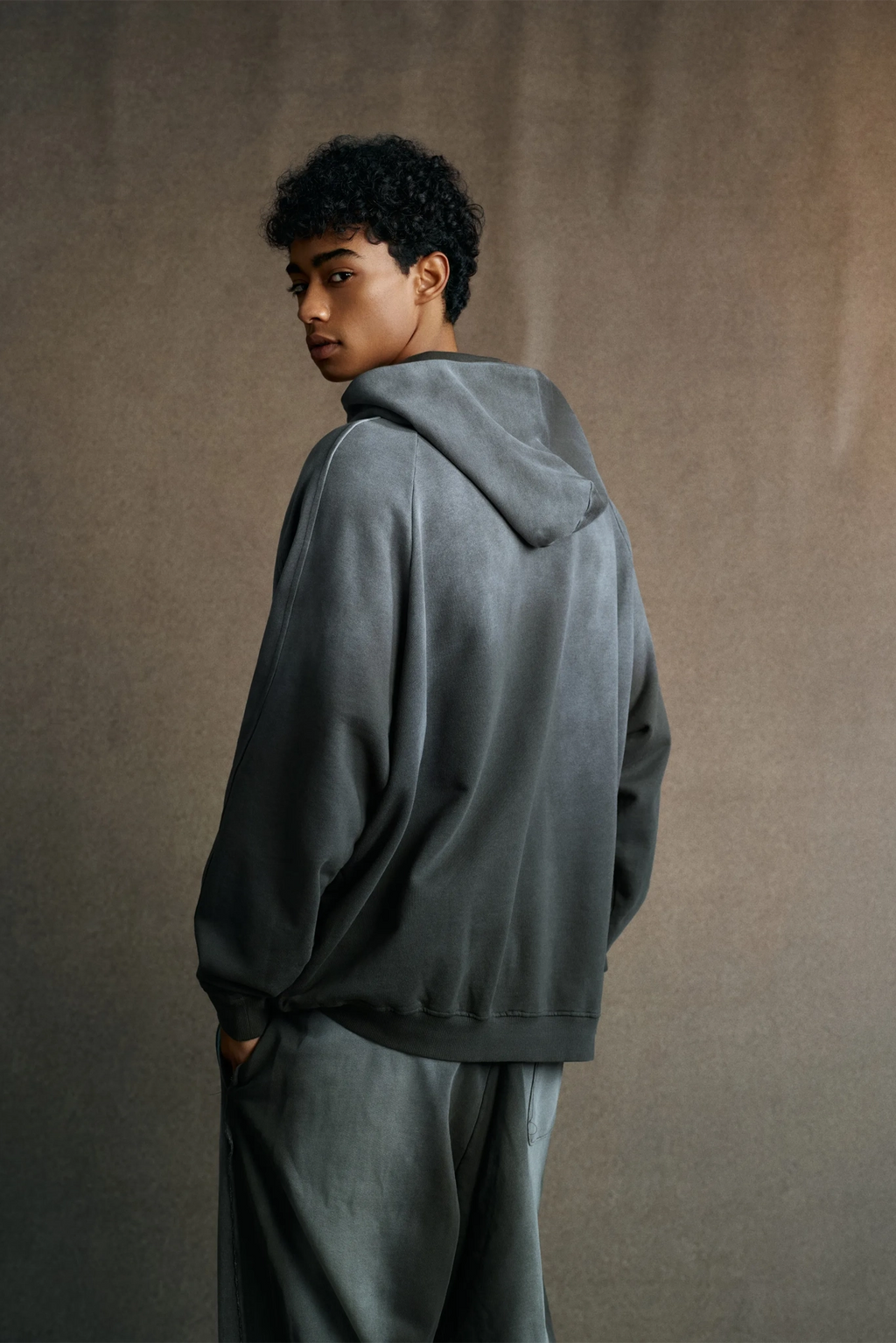 Person wearing a gray hoodie and pants against a brown background