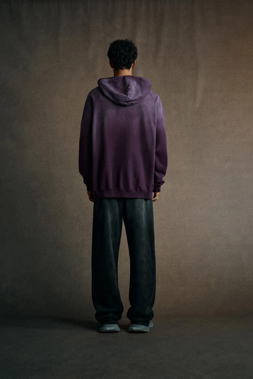 Person wearing a purple hoodie and dark pants standing against a plain background