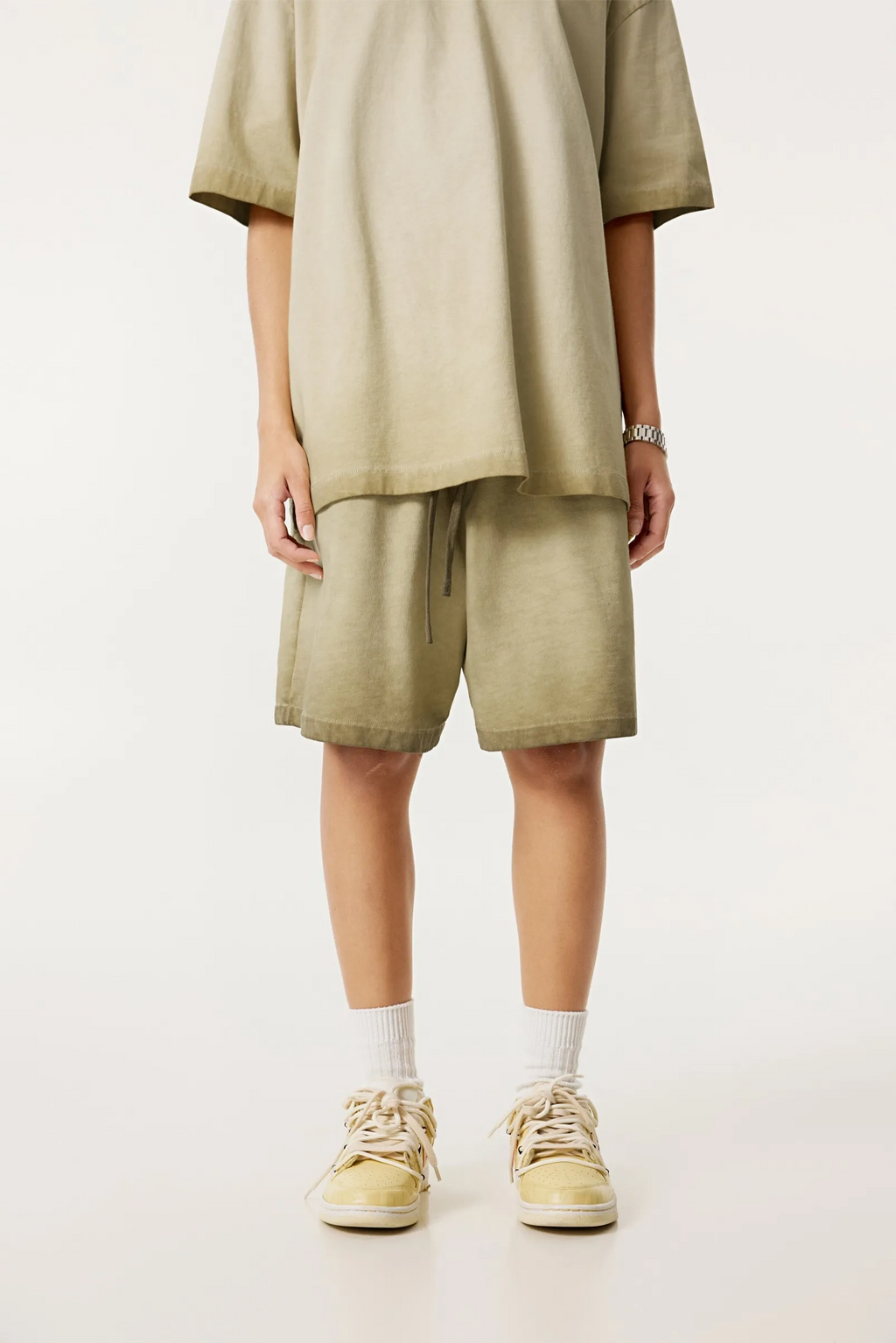 Person wearing a beige outfit with shorts and sneakers on a white background