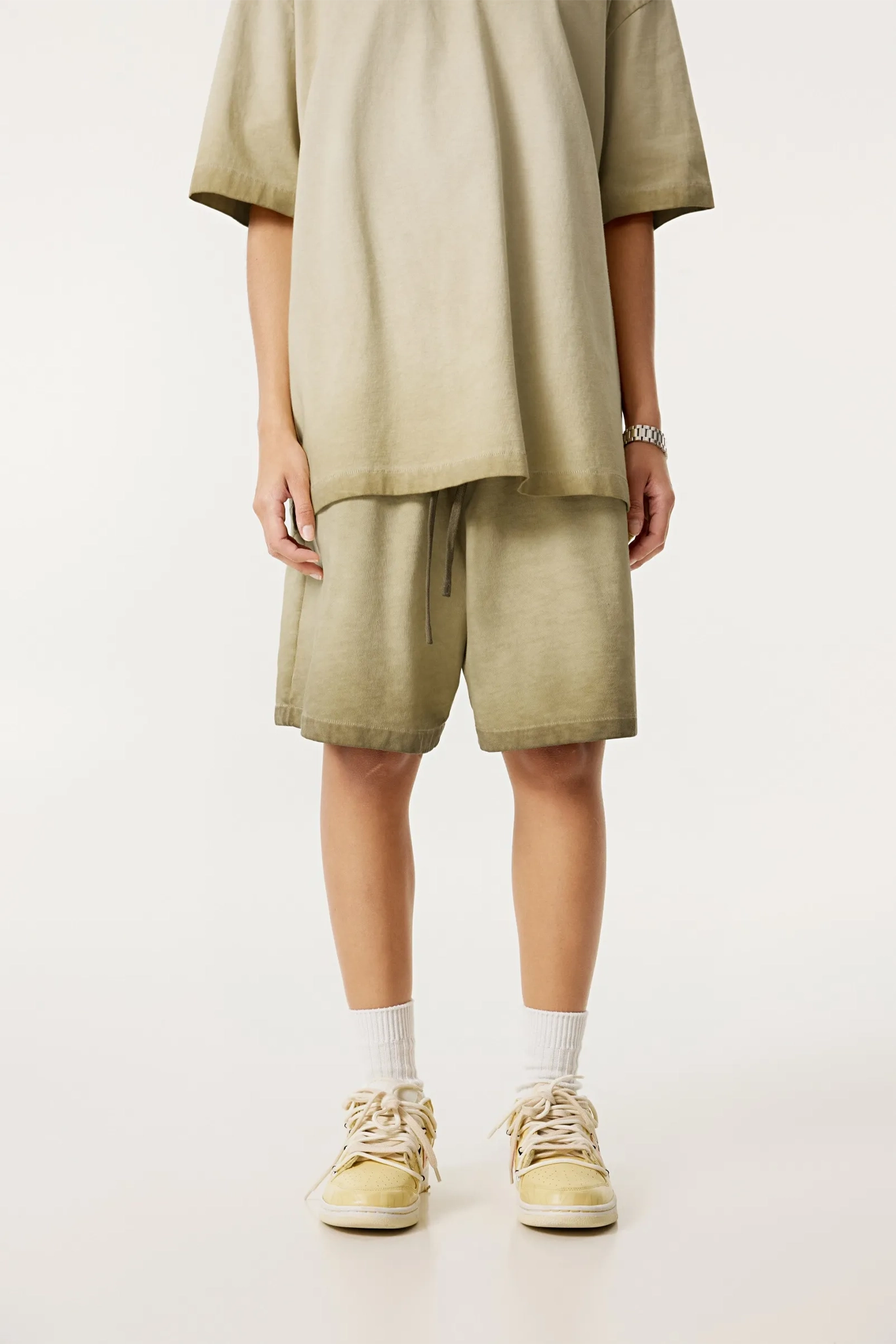 Person wearing a beige outfit with shorts and sneakers on a white background