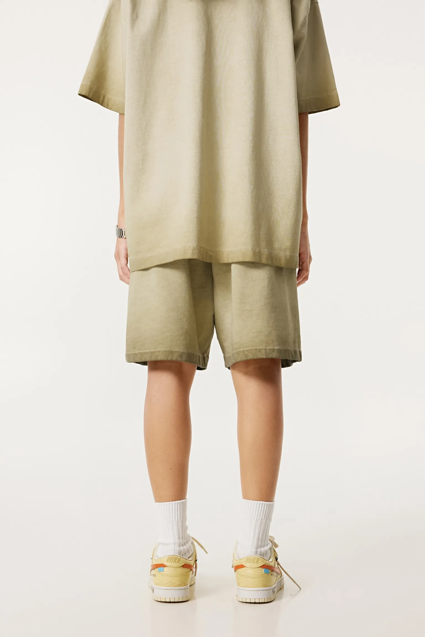 Person wearing a beige outfit with shorts and a shirt on a white background