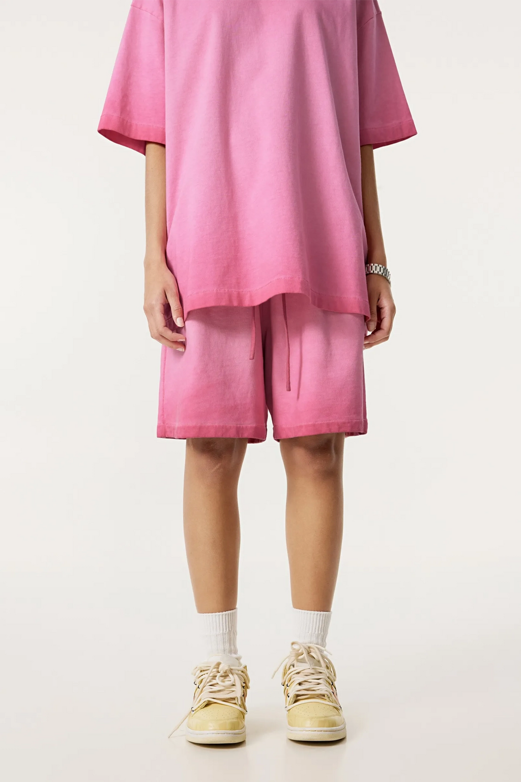 Person wearing a pink outfit with shorts and a loose-fitting top on a white background