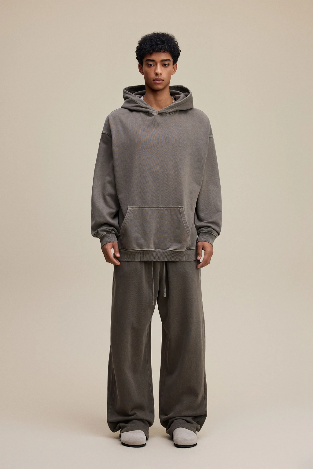 Person wearing a gray hoodie and pants on a beige background