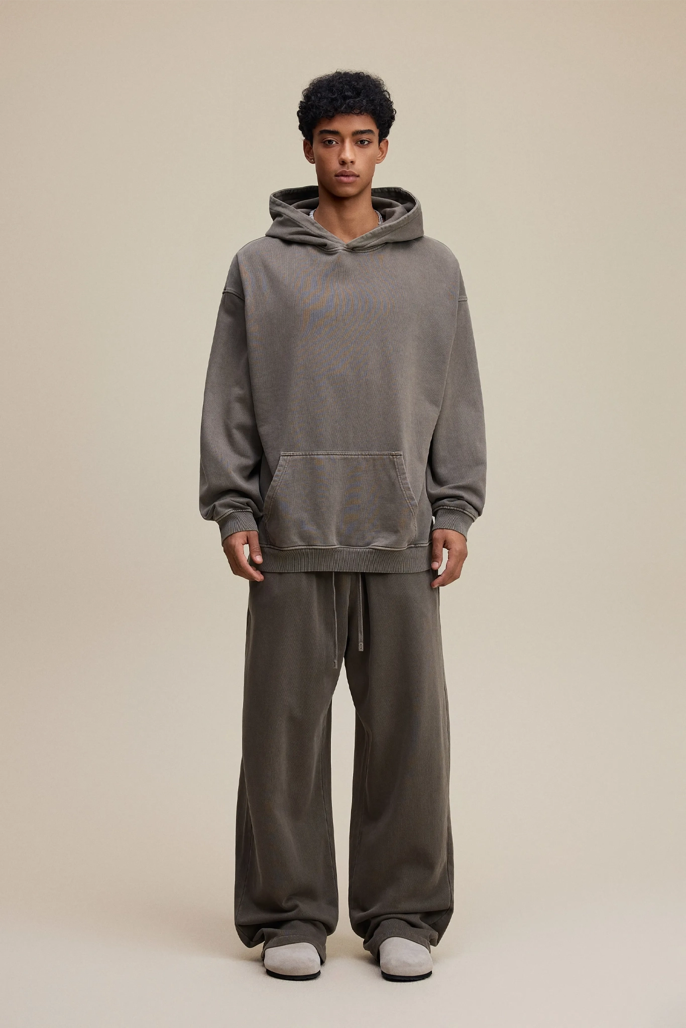 Person wearing a gray hoodie and pants on a beige background