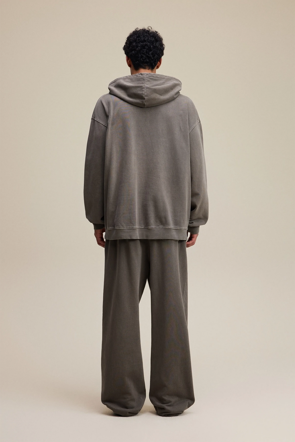 Person wearing a gray hoodie and pants on a beige background