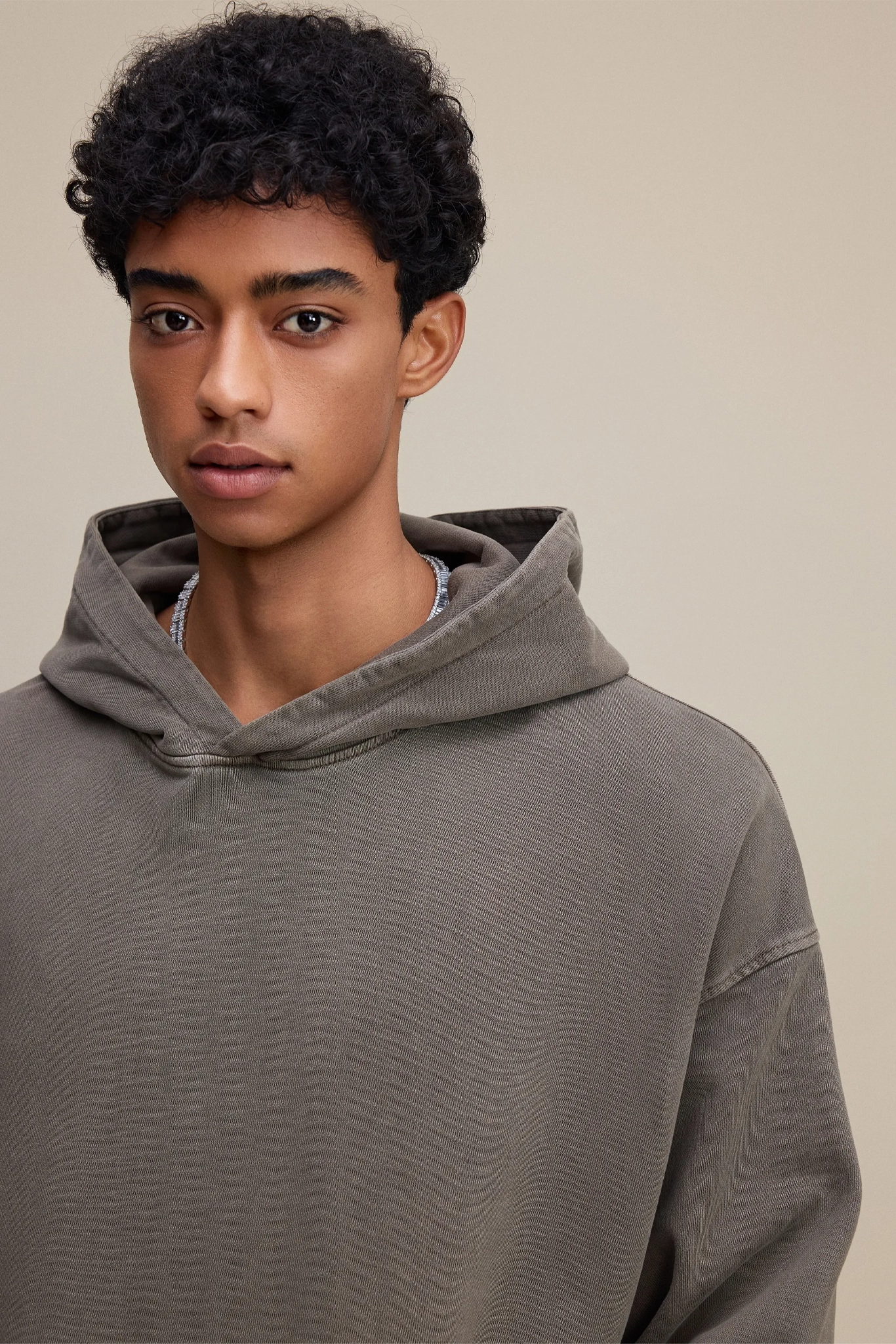 Person wearing a gray hoodie against a beige background