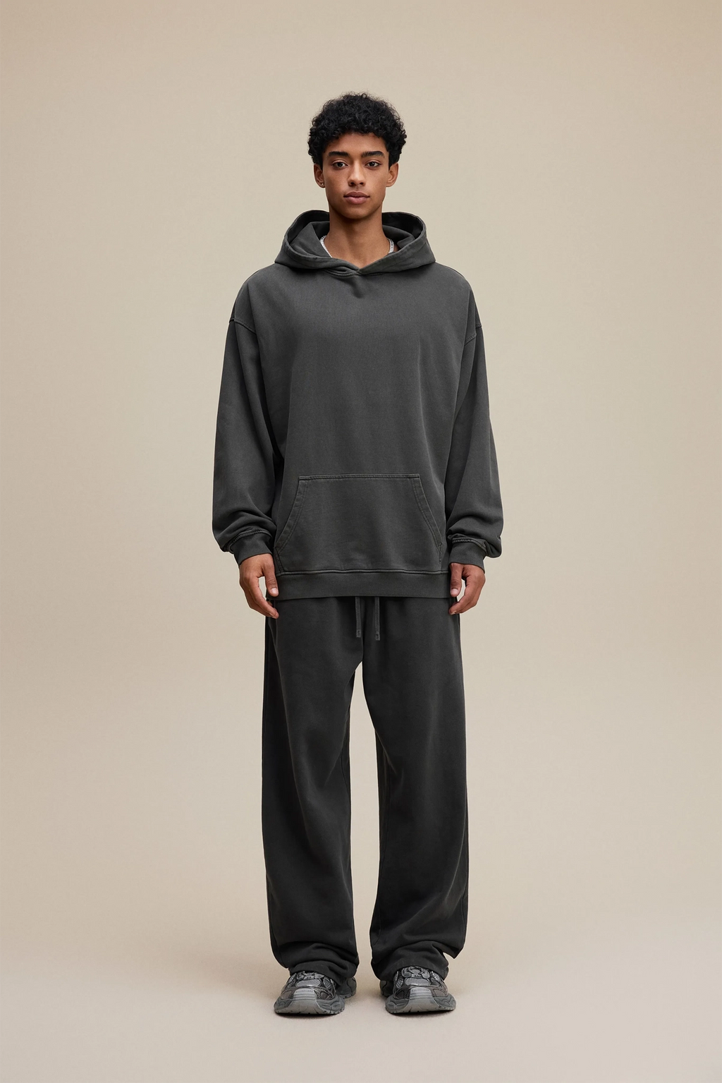 Person wearing a dark gray hoodie and pants on a beige background