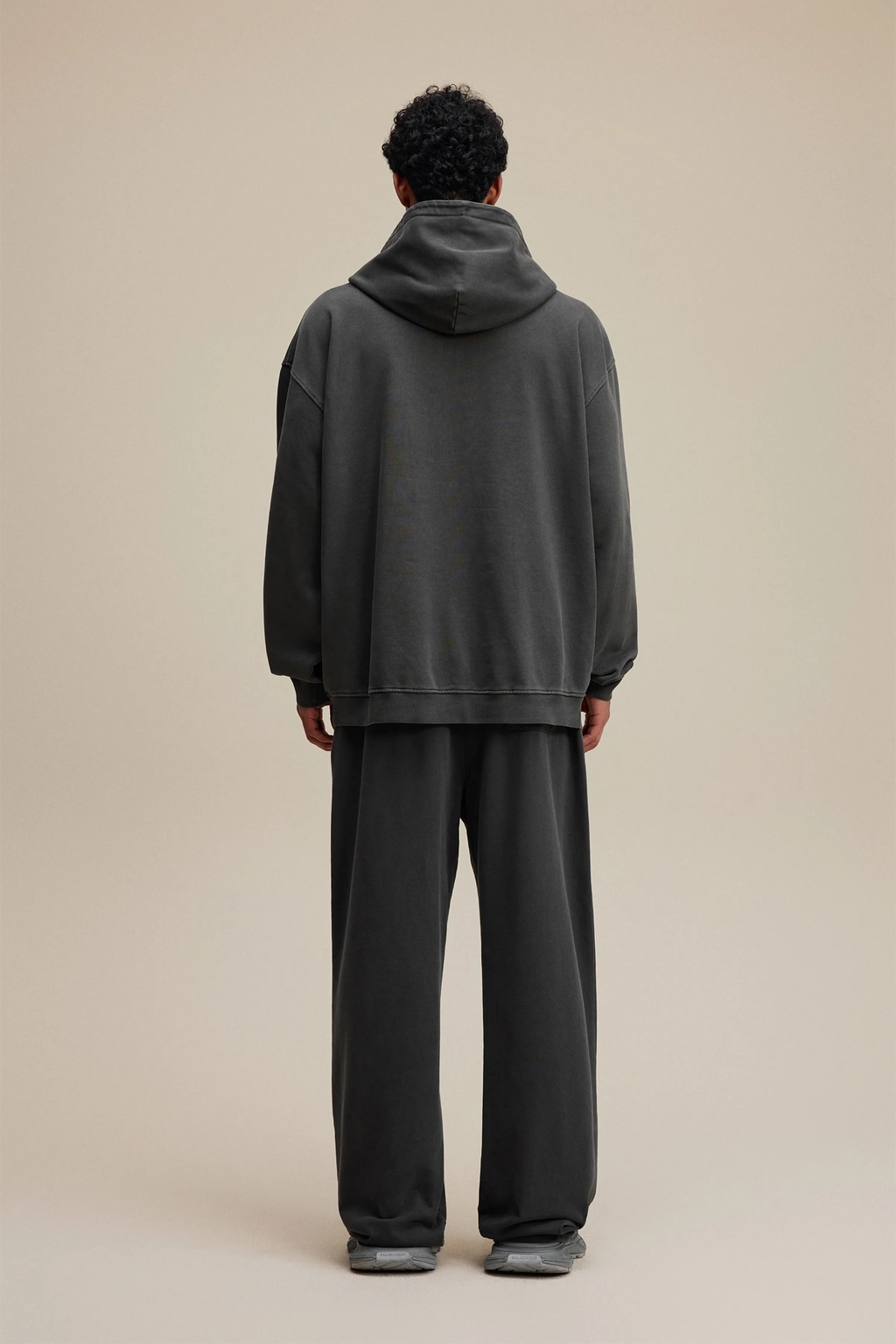 Person wearing a dark gray hoodie and pants on a beige background