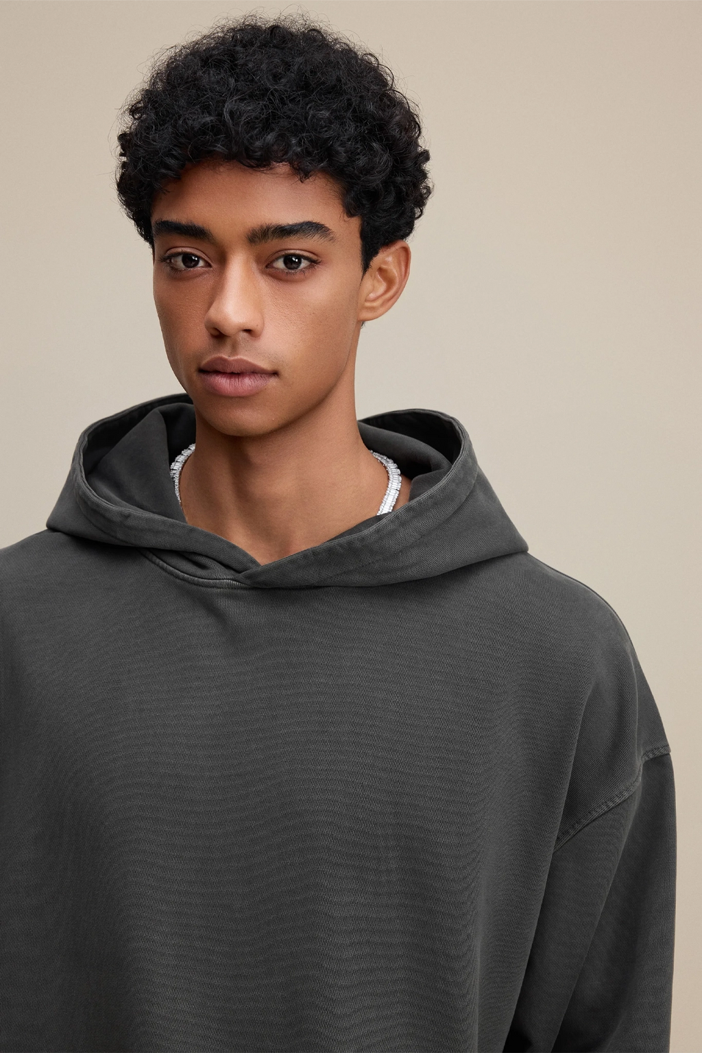 Person wearing a dark gray hoodie against a beige background