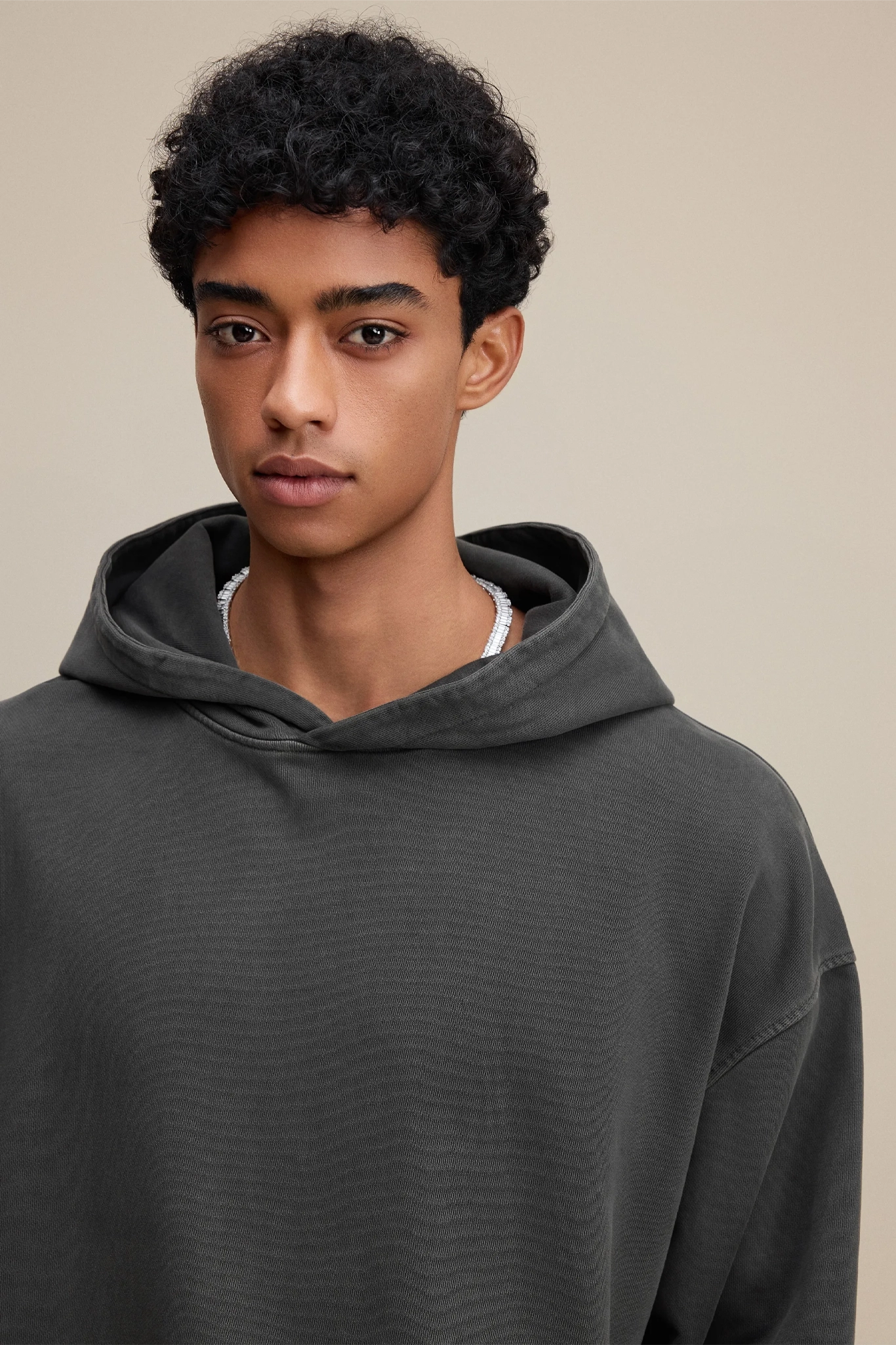 Person wearing a dark gray hoodie against a beige background
