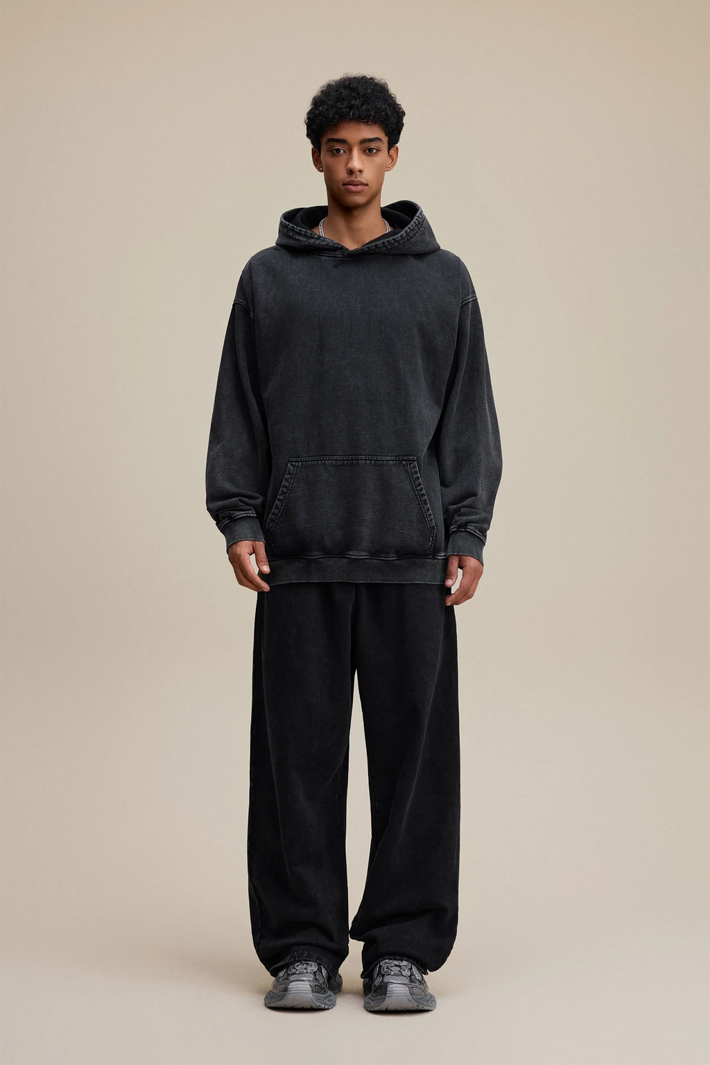 Person wearing a black hoodie and pants on a beige background